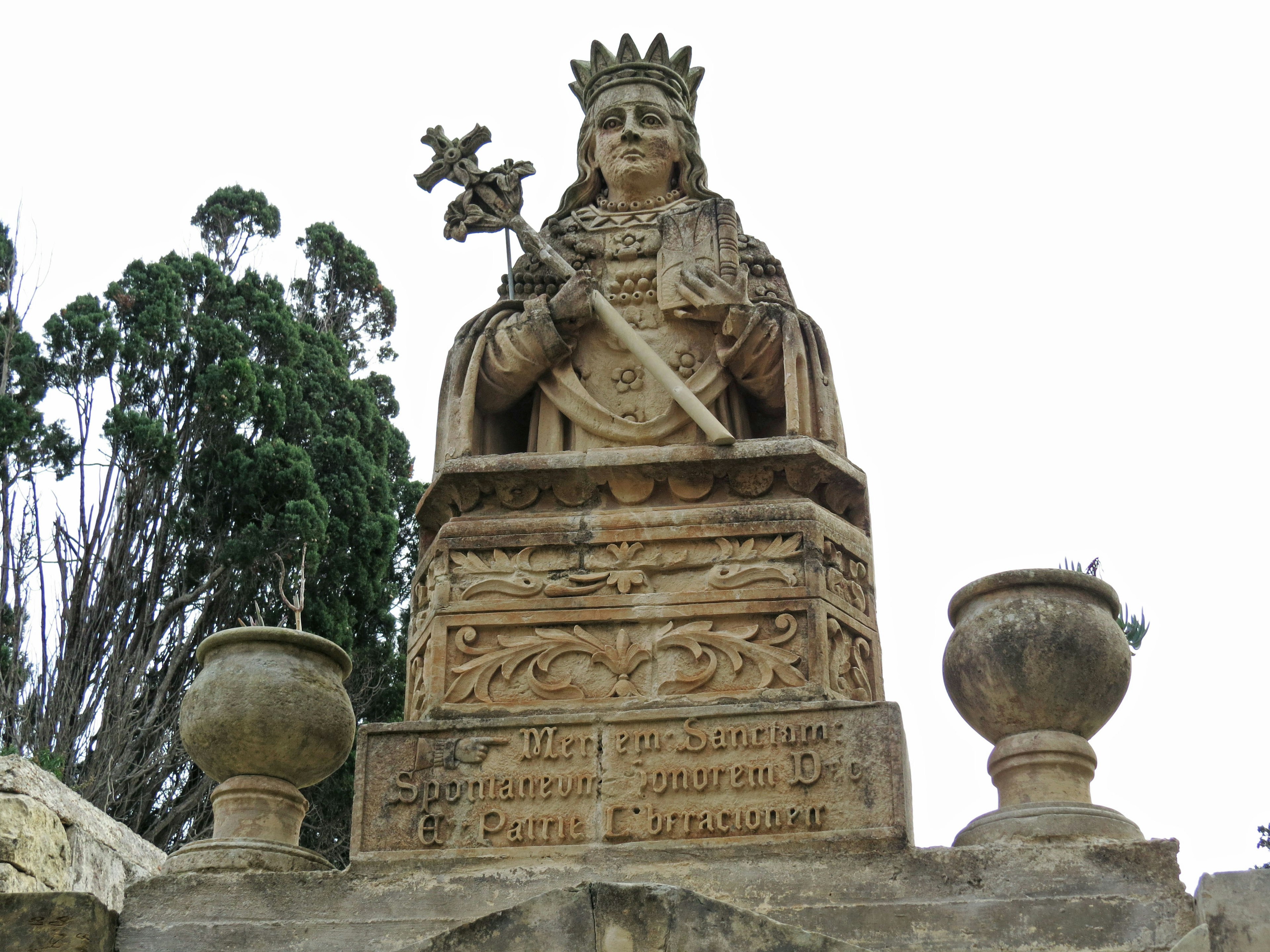 Statue en pierre d'une femme couronnée tenant une croix sur un piédestal