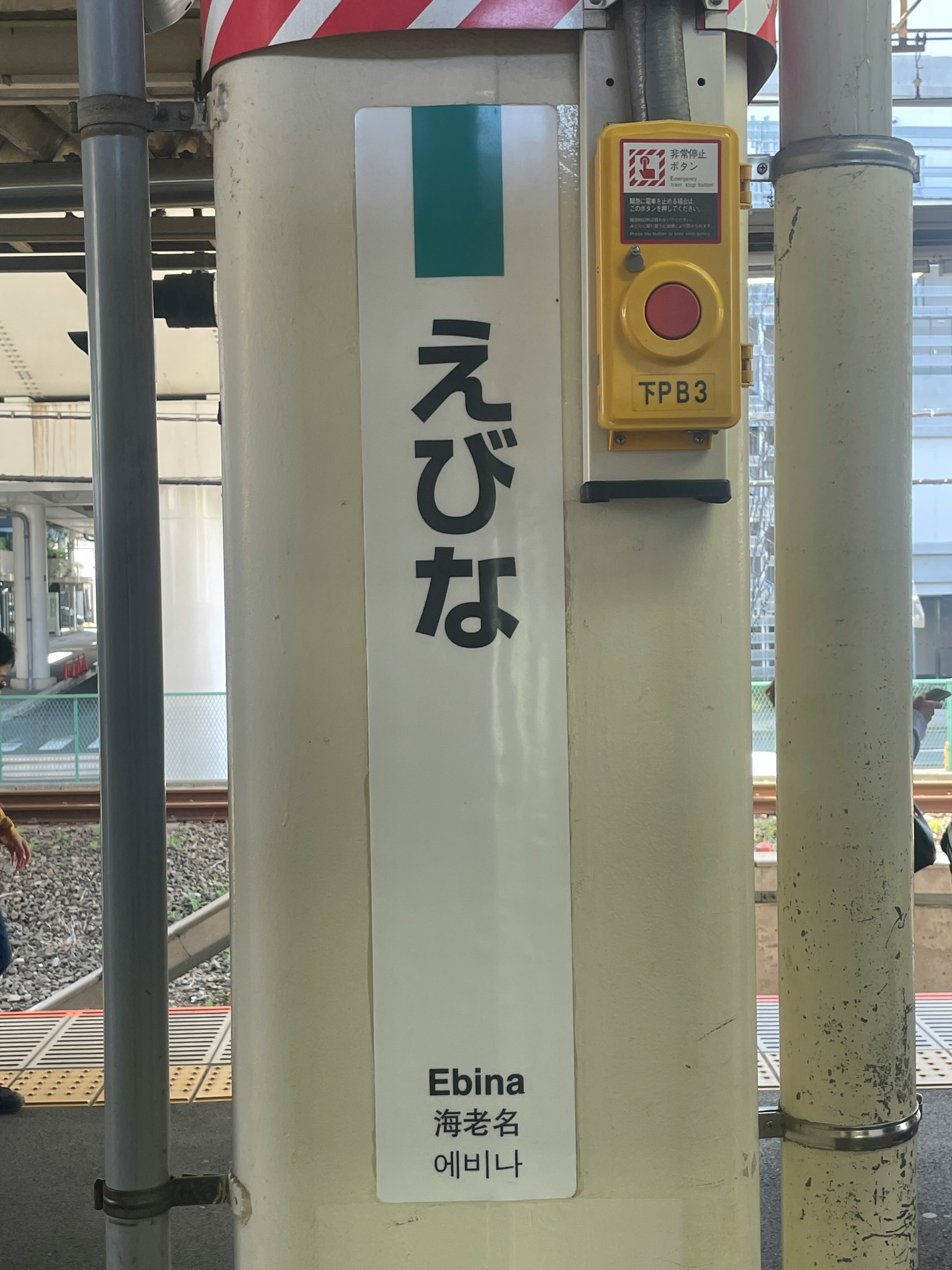 Bahnhofsschild für Ebina mit einem Knopf am Pfeiler