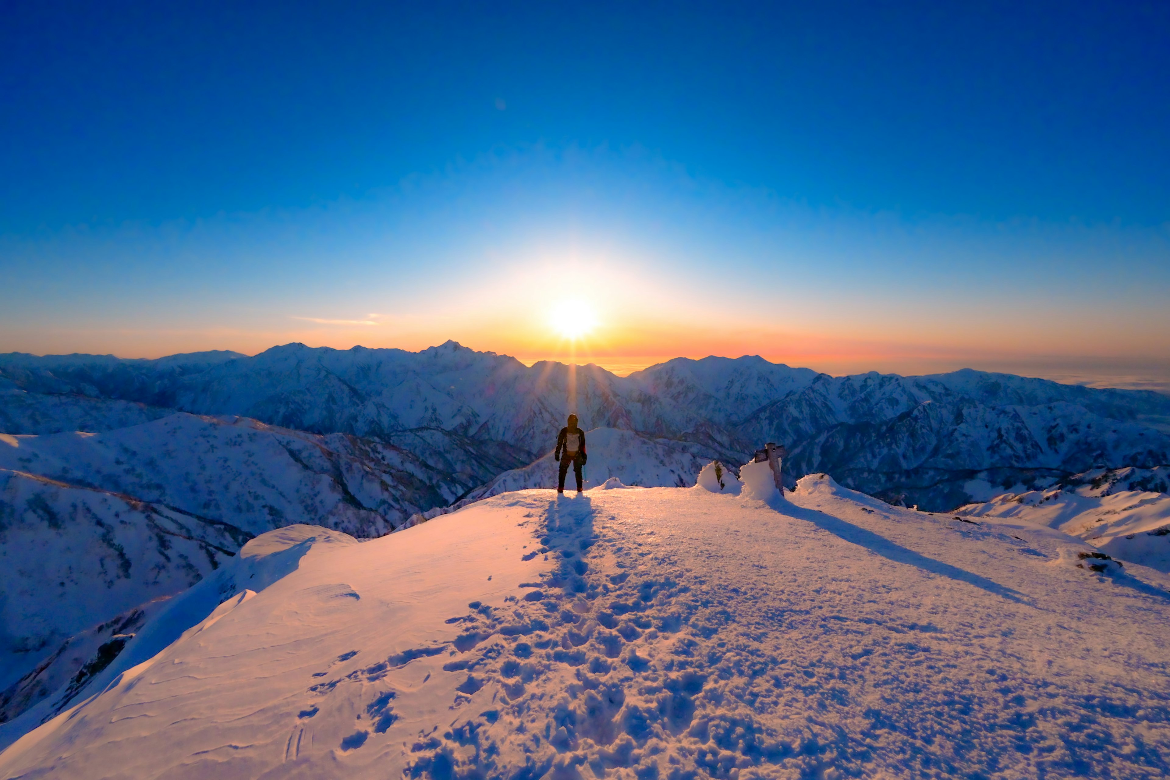 雪に覆われた山の頂上で日の出を眺める登山者のシルエット