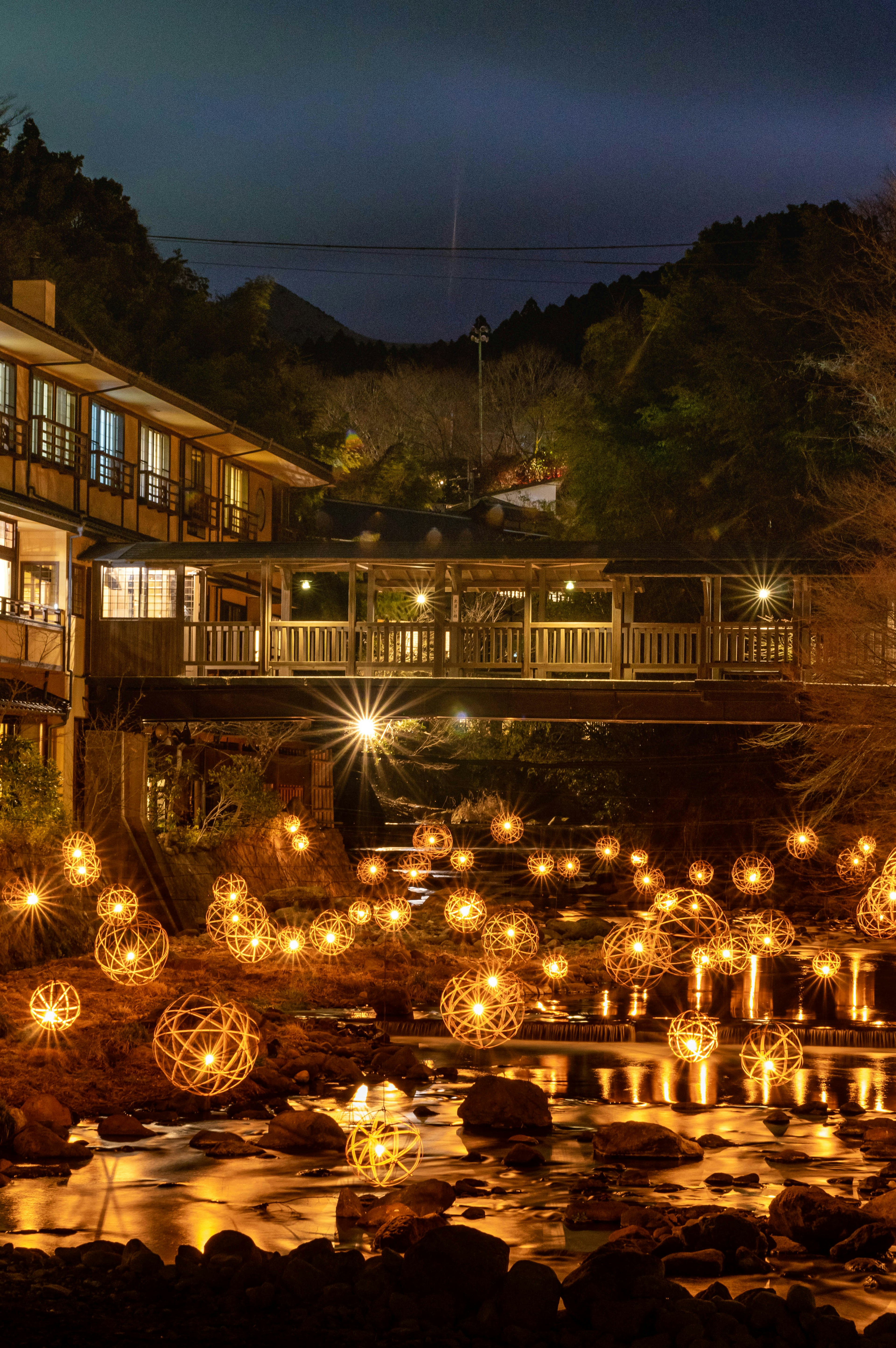 Vue pittoresque d'une auberge de sources chaudes avec des lanternes flottant sur la rivière la nuit