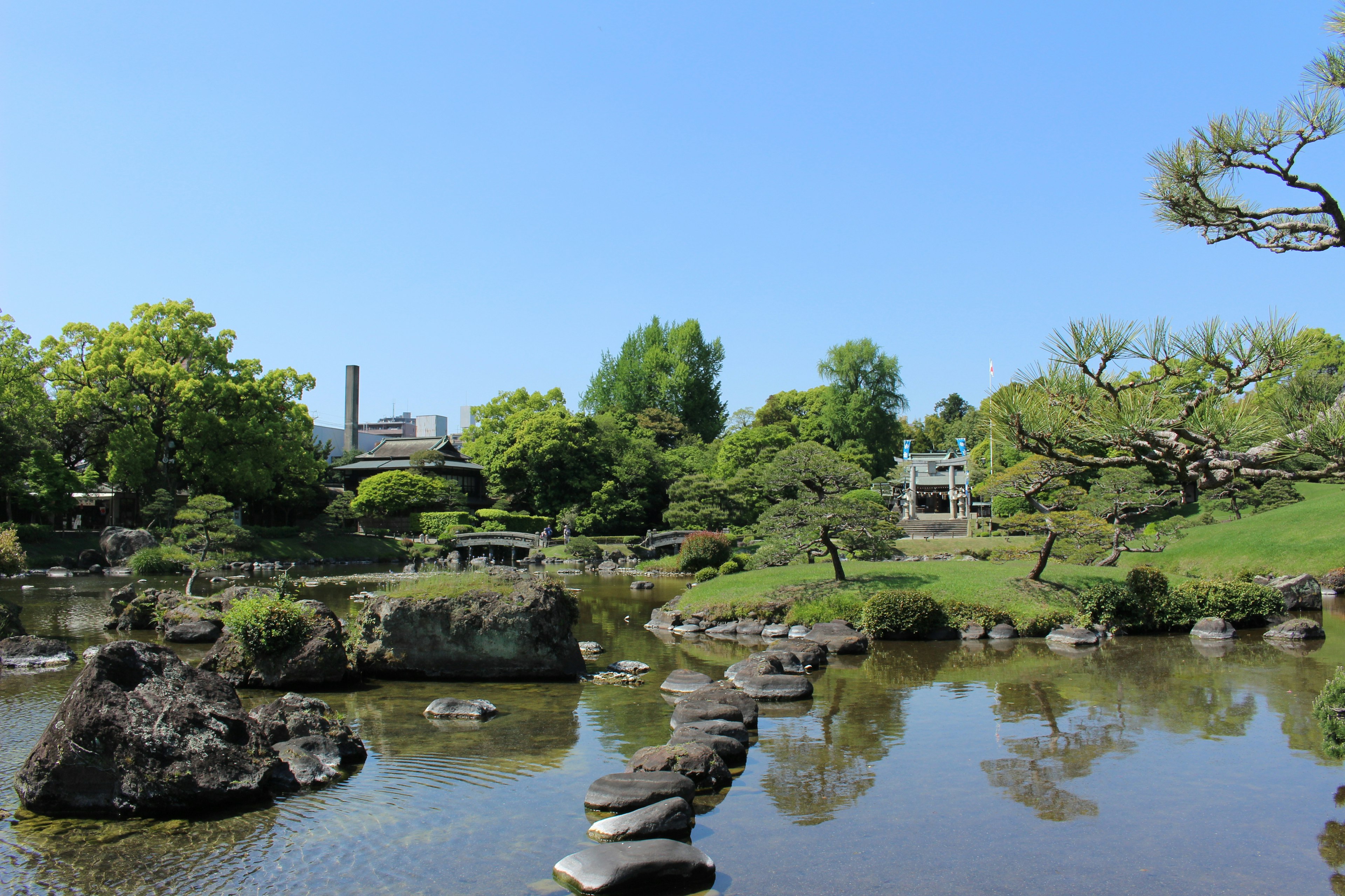 Pemandangan taman Jepang yang tenang Jalur batu melintasi kolam Vegetasi subur dan langit biru