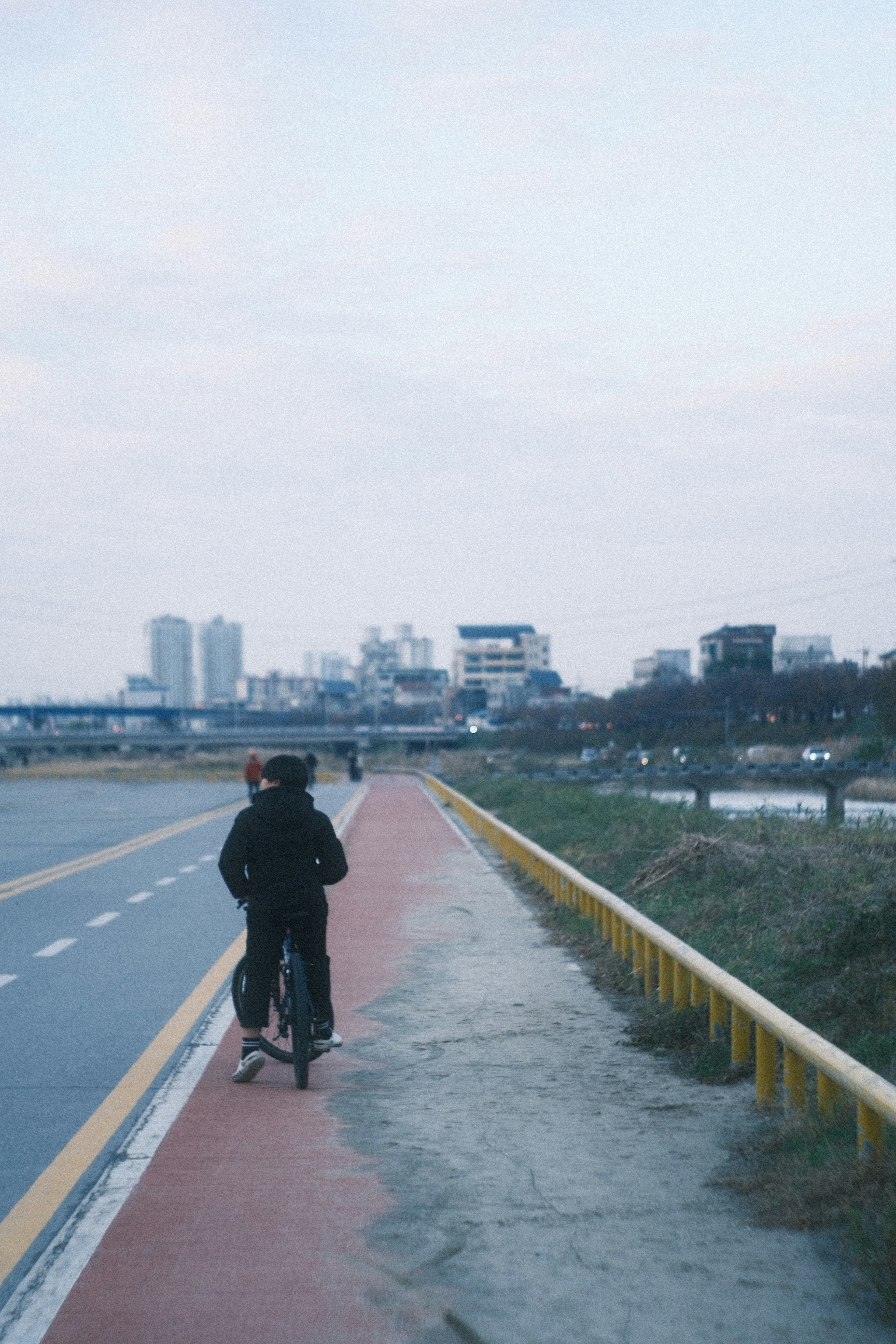 自転車に乗る人が都市の景色を背景にした川沿いの道を走っている