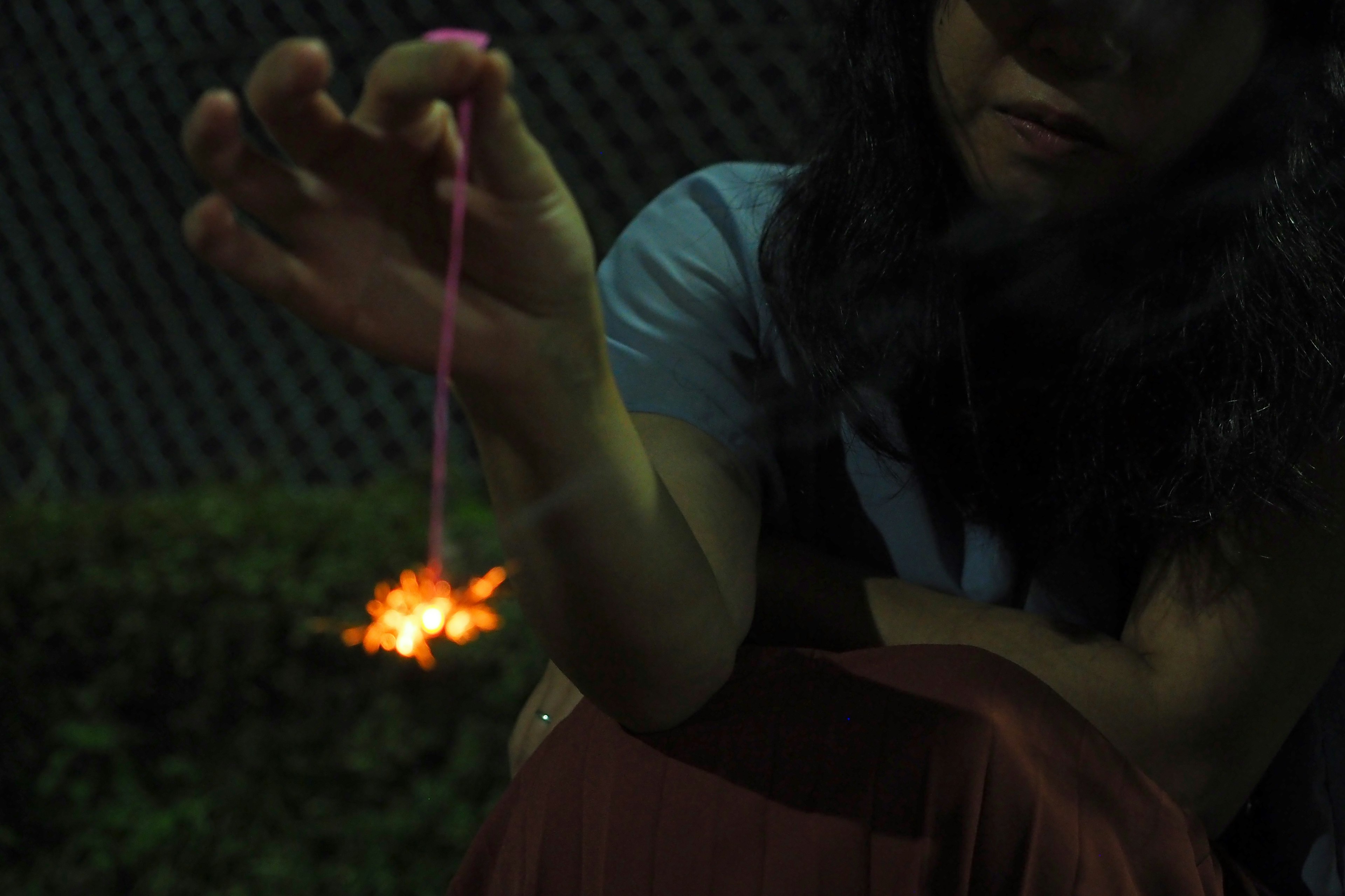 Una mujer sosteniendo un fuego artificial con chispas brillantes sobre un fondo oscuro