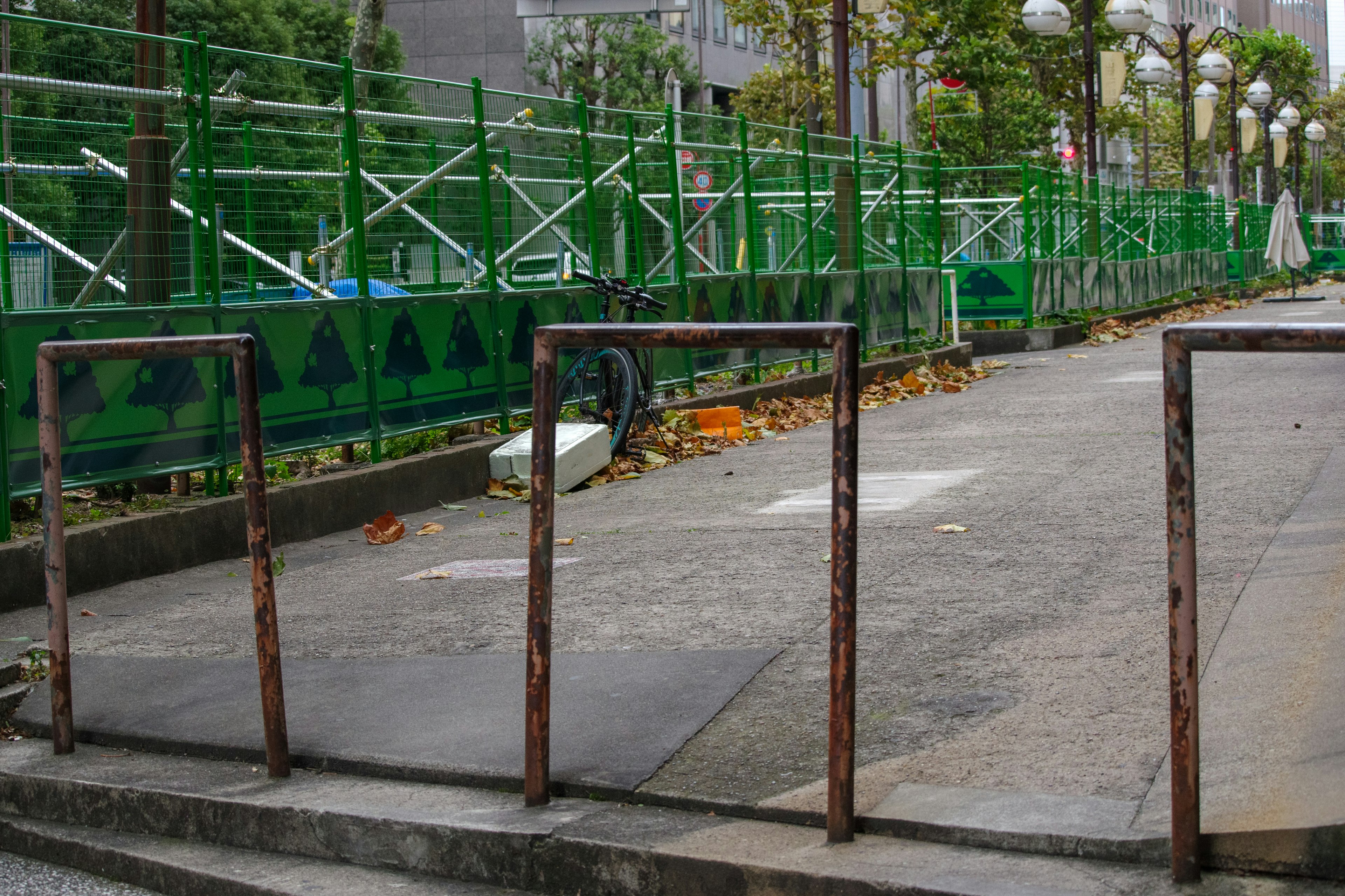 Sidewalk with rusty metal frames surrounding a green fence