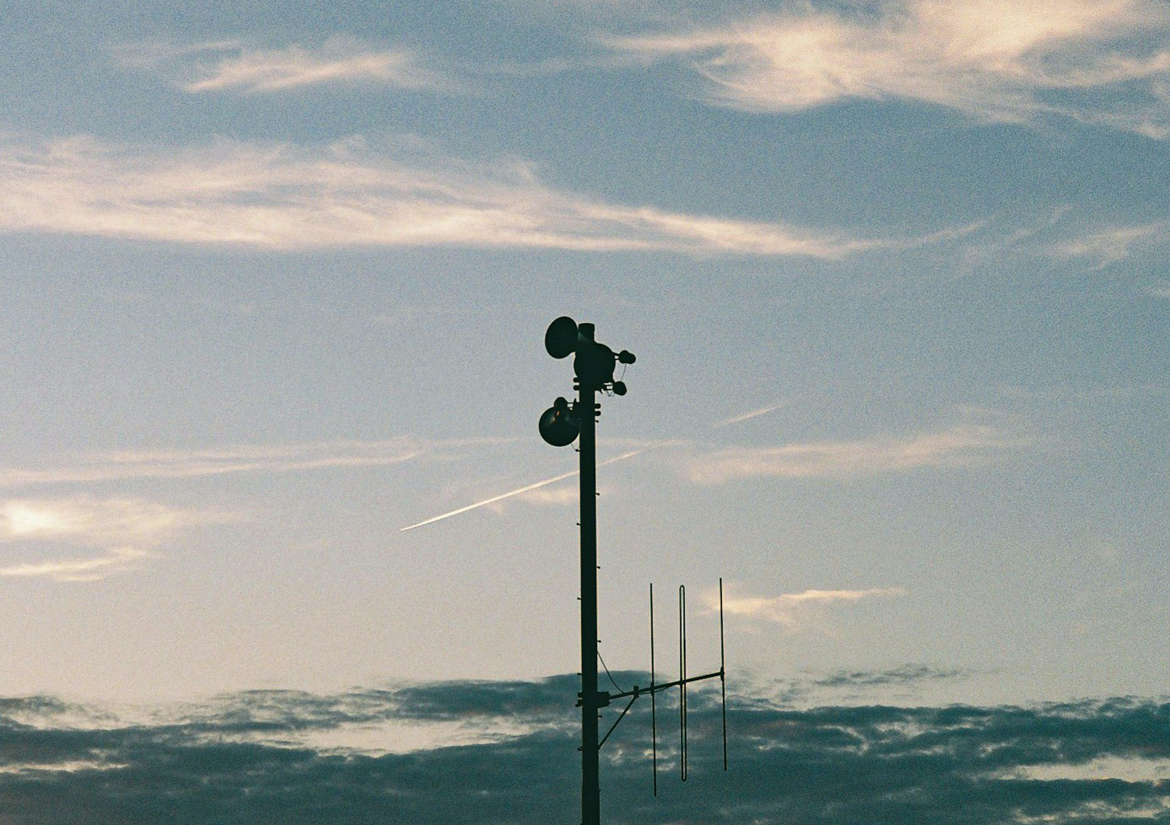 Silhouette of a communication tower with speakers against a blue sky