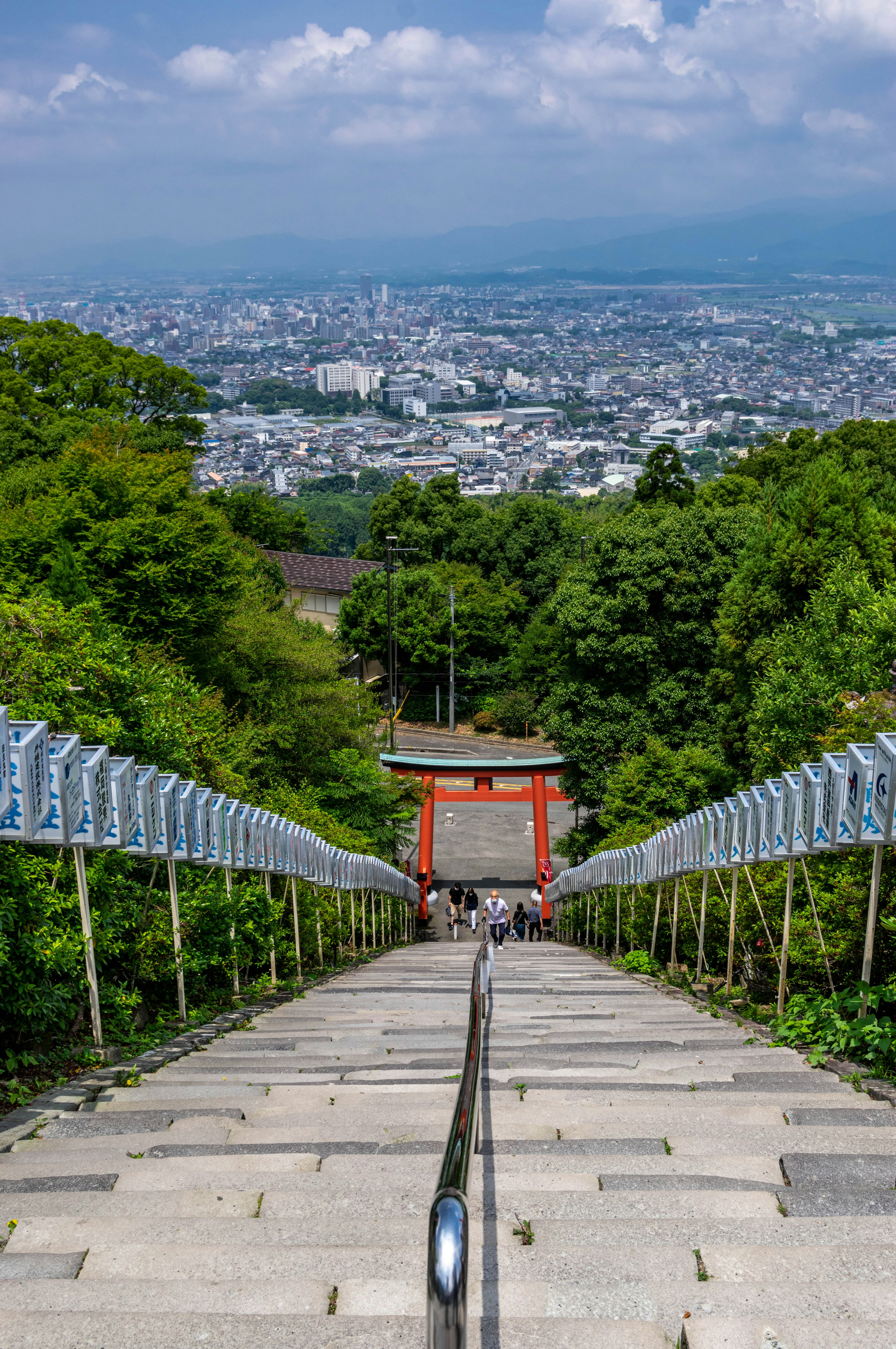 緑に囲まれた階段が続く風景の中に赤い鳥居が見える