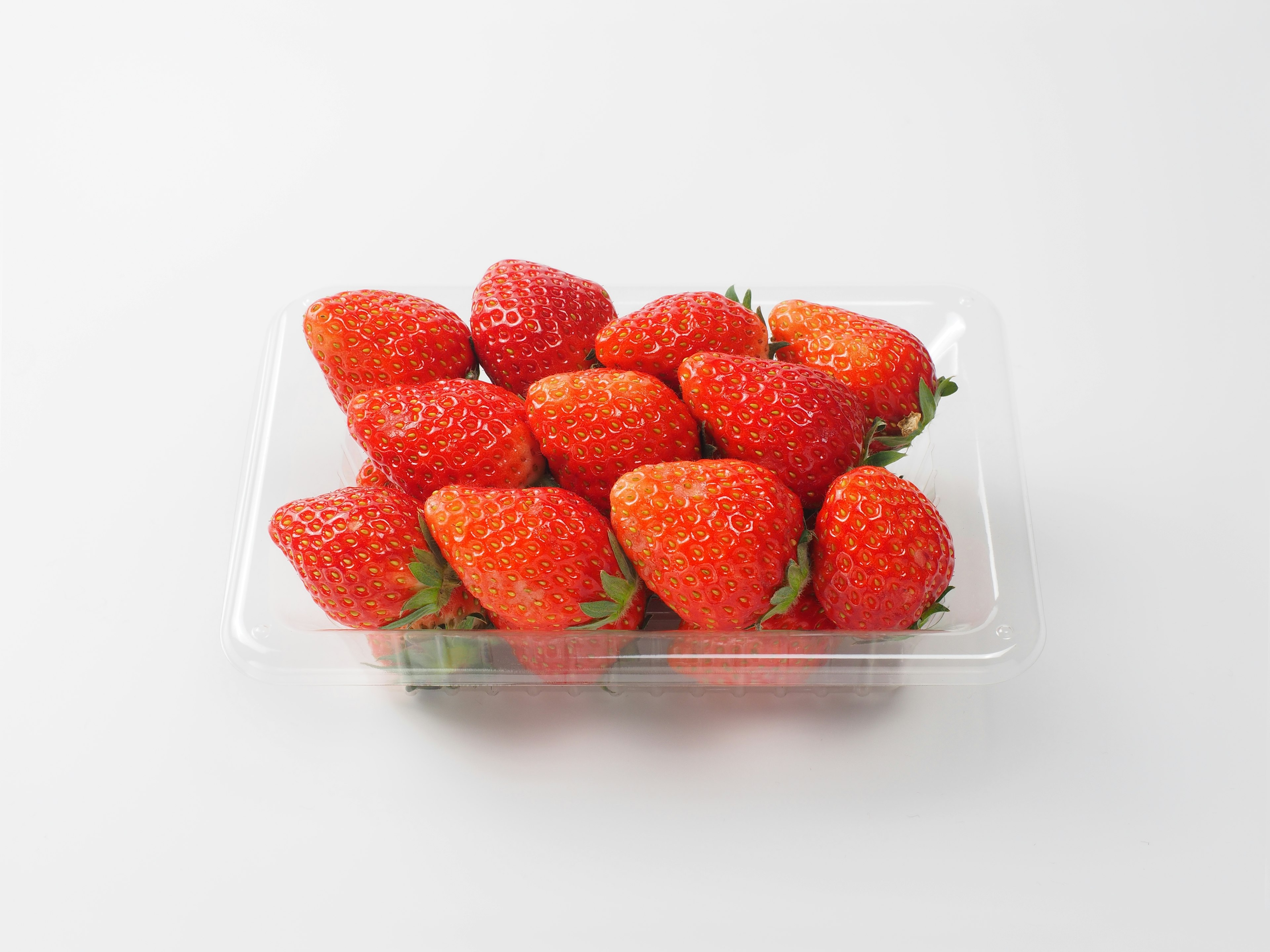 A clear plastic container filled with vibrant red strawberries