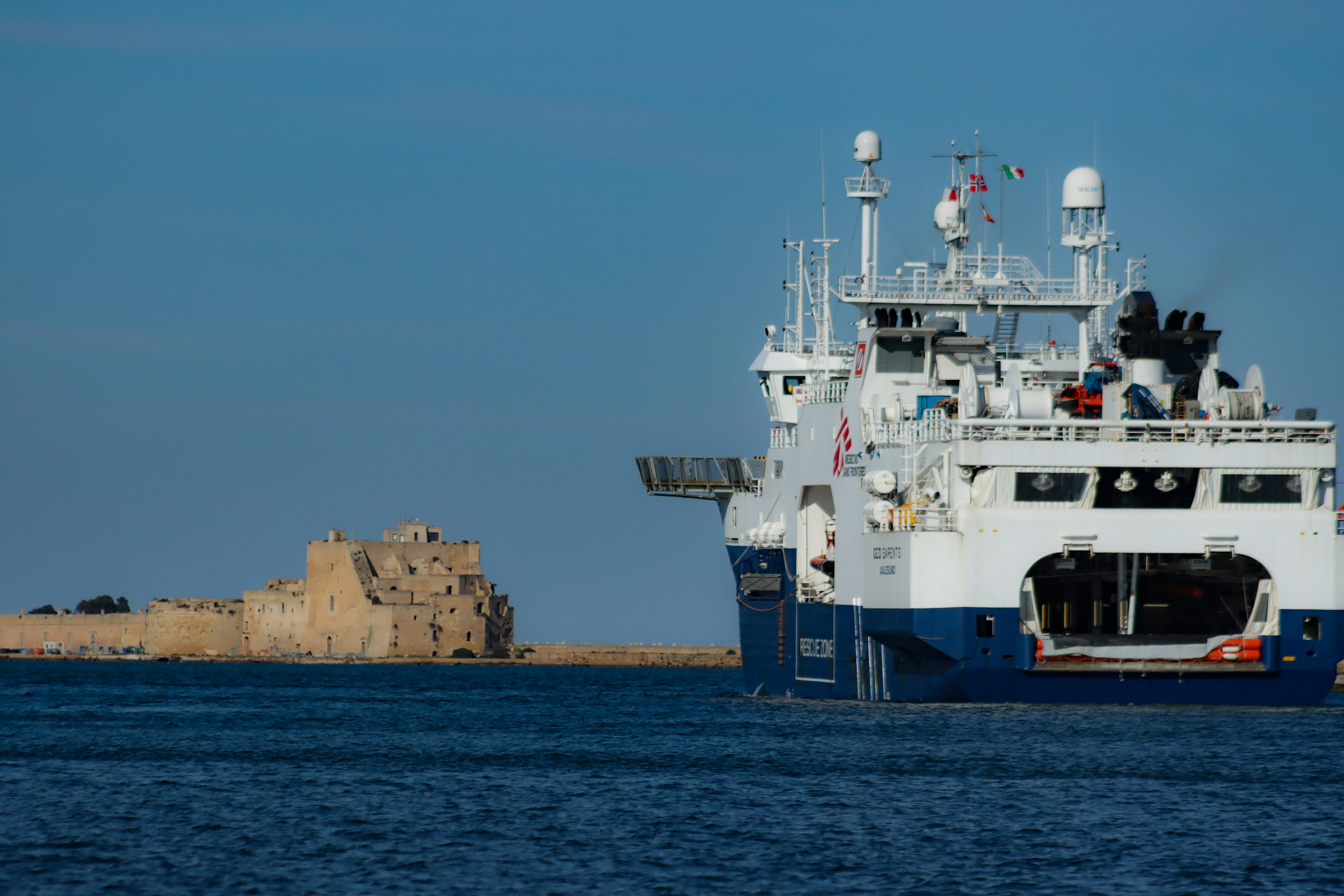 Grand navire ancré dans une mer bleue avec une île rocheuse au loin