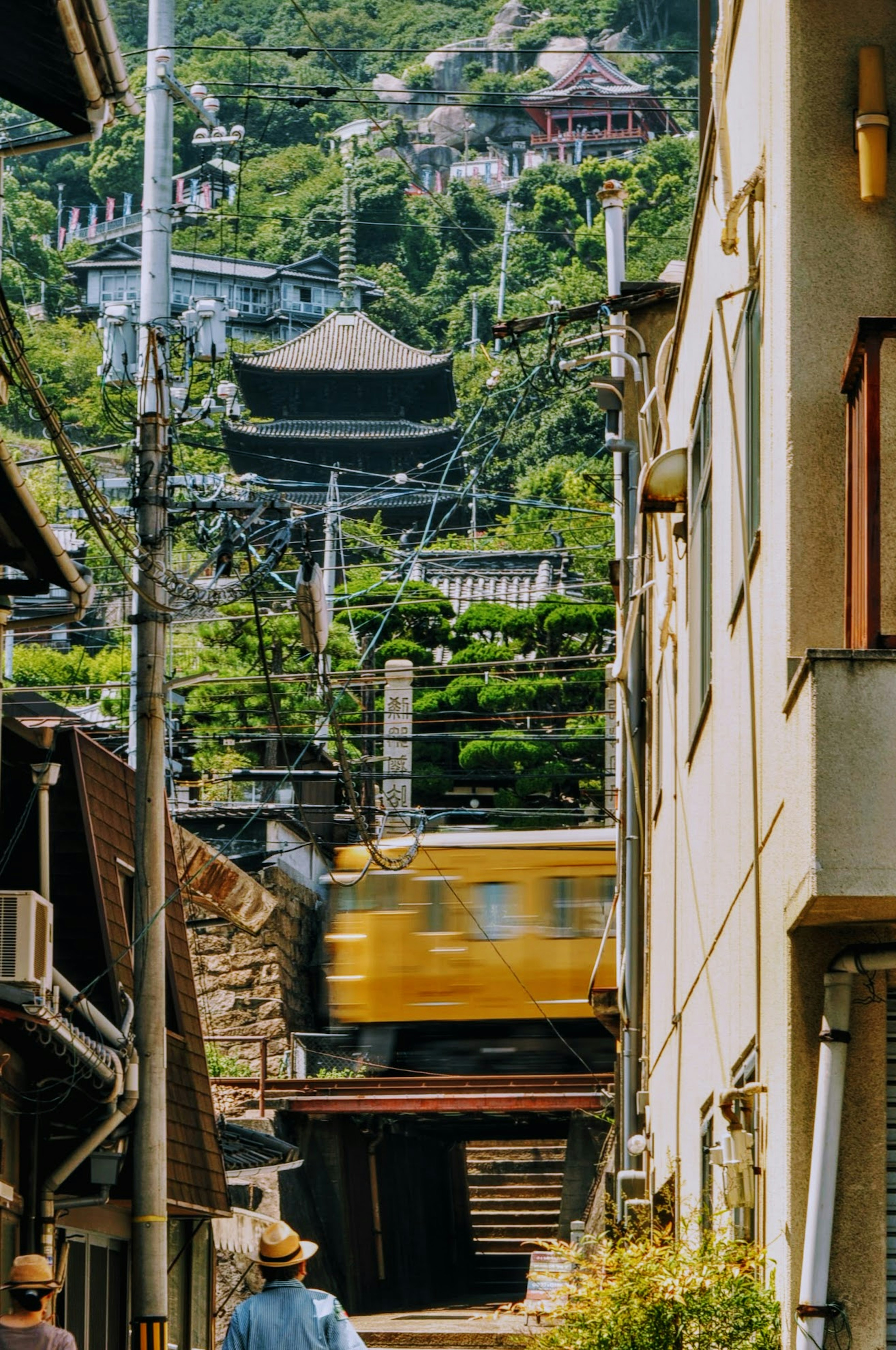 Imagen de un callejón estrecho con un tren amarillo pasando frente a un paisaje montañoso