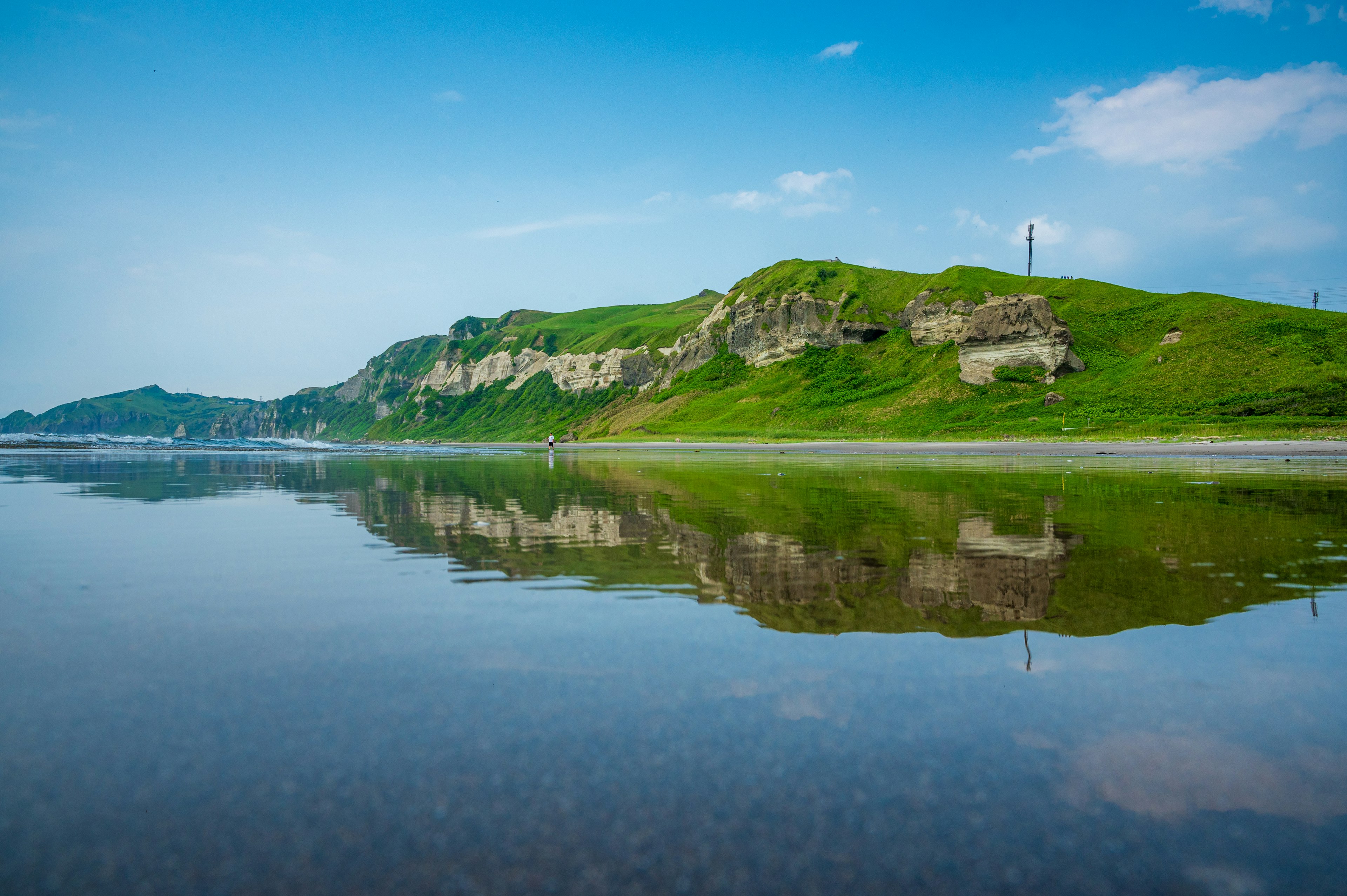 Calm beach showcasing reflection of green hills under a blue sky