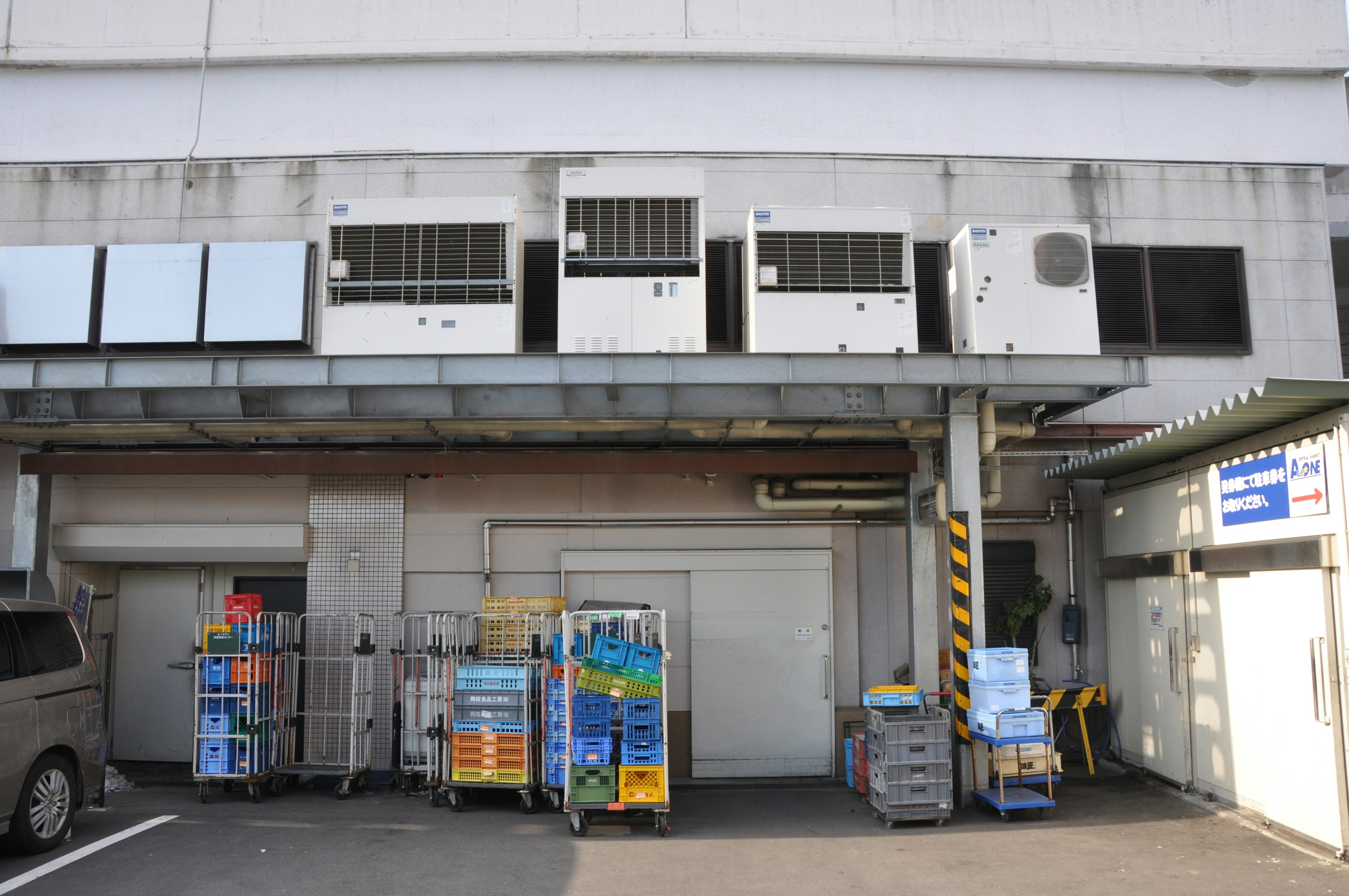 Exterior of a building with multiple air conditioning units and carts stacked with goods near the warehouse entrance