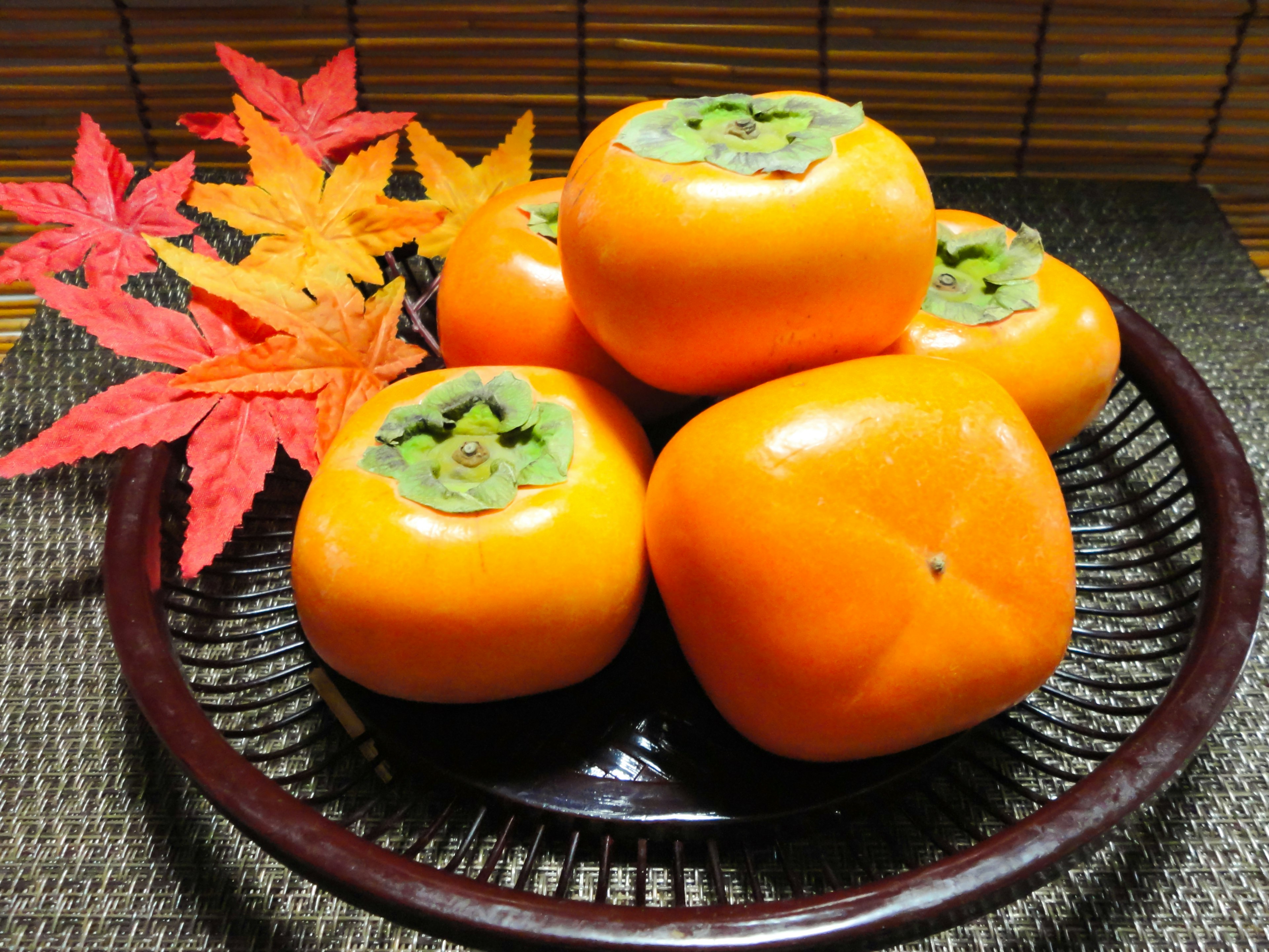 A bowl of vibrant orange persimmons alongside autumn leaves