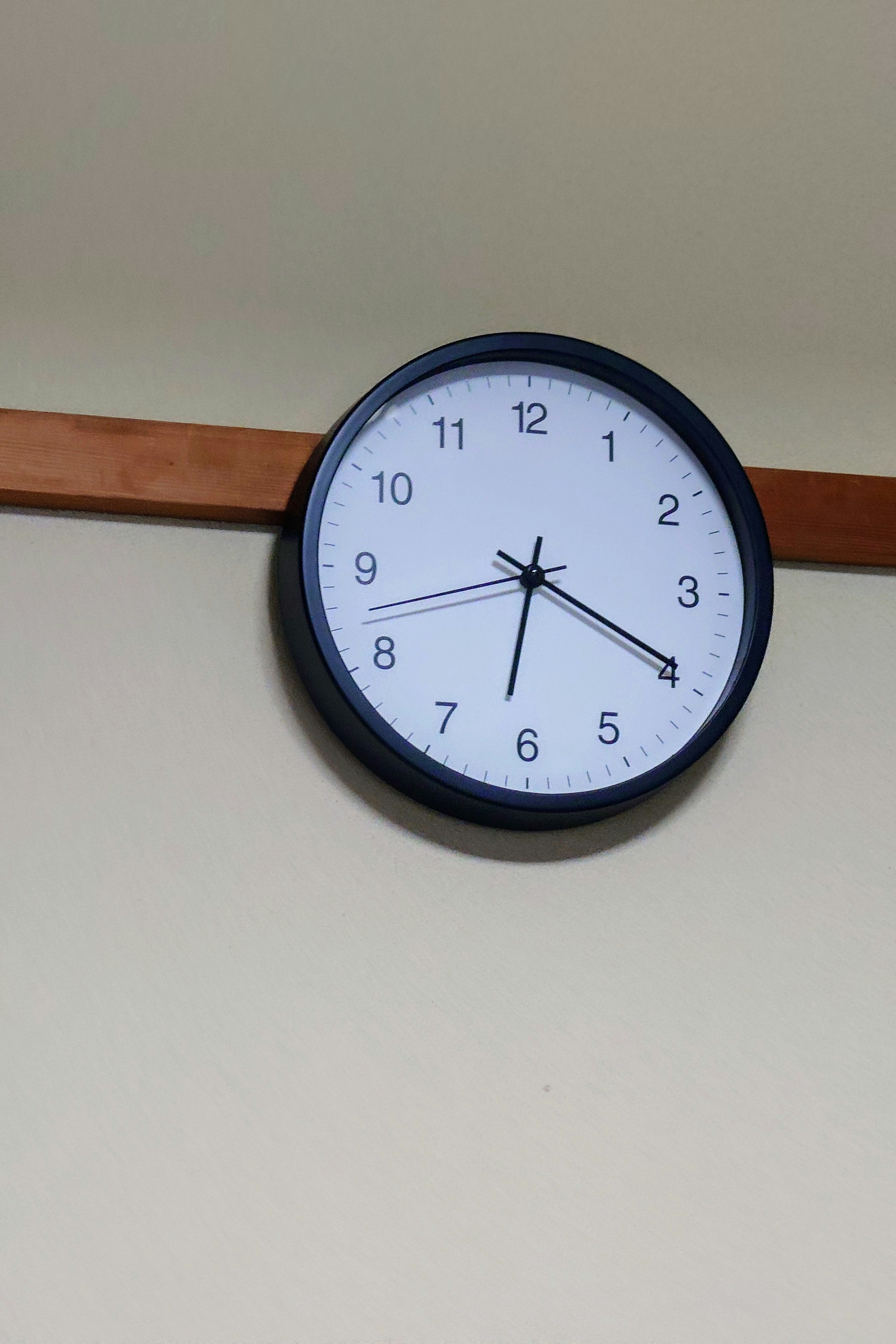 Black wall clock with white face hanging on a wooden beam