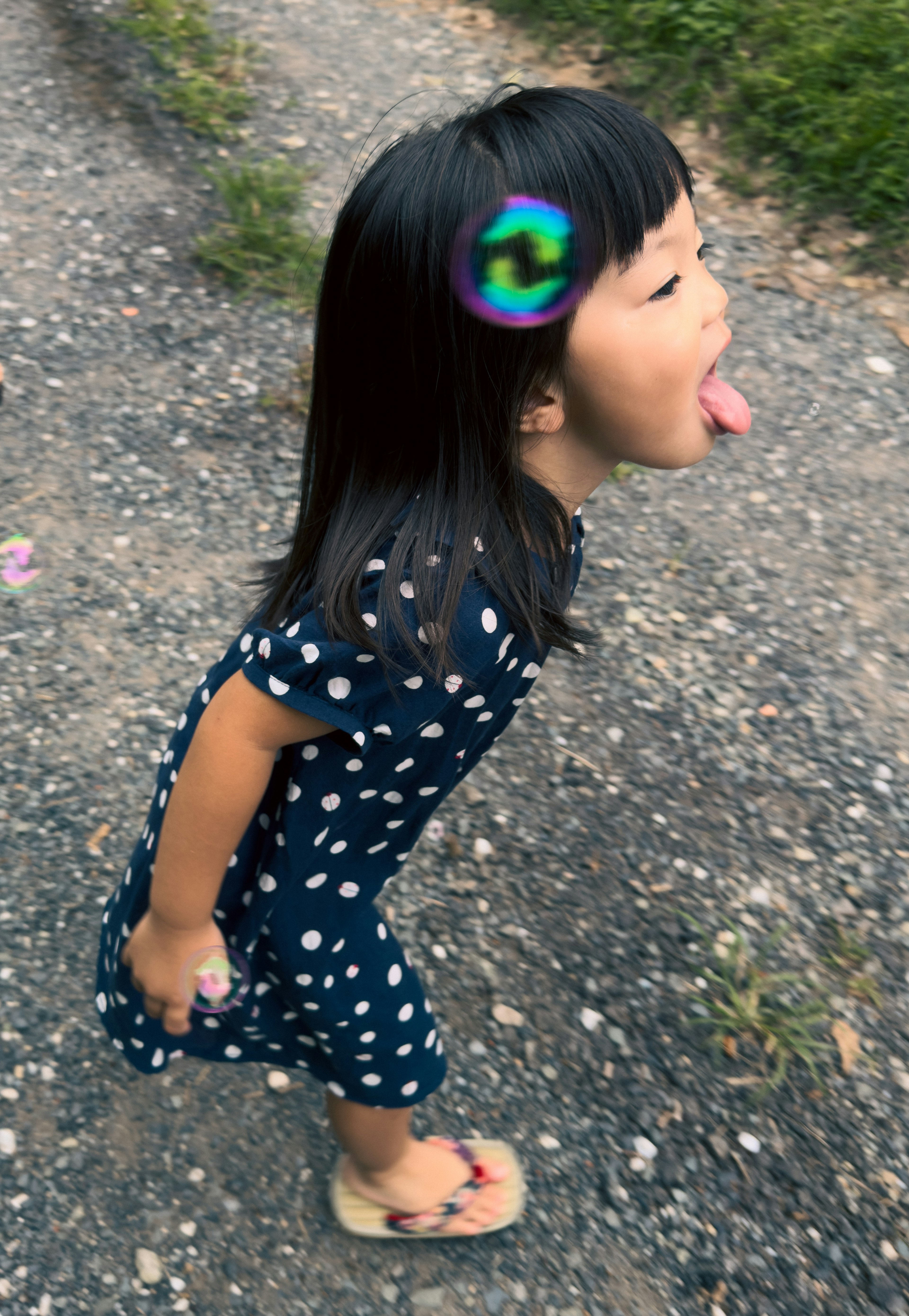 Child standing on a path wearing a polka dot dress sticking out her tongue