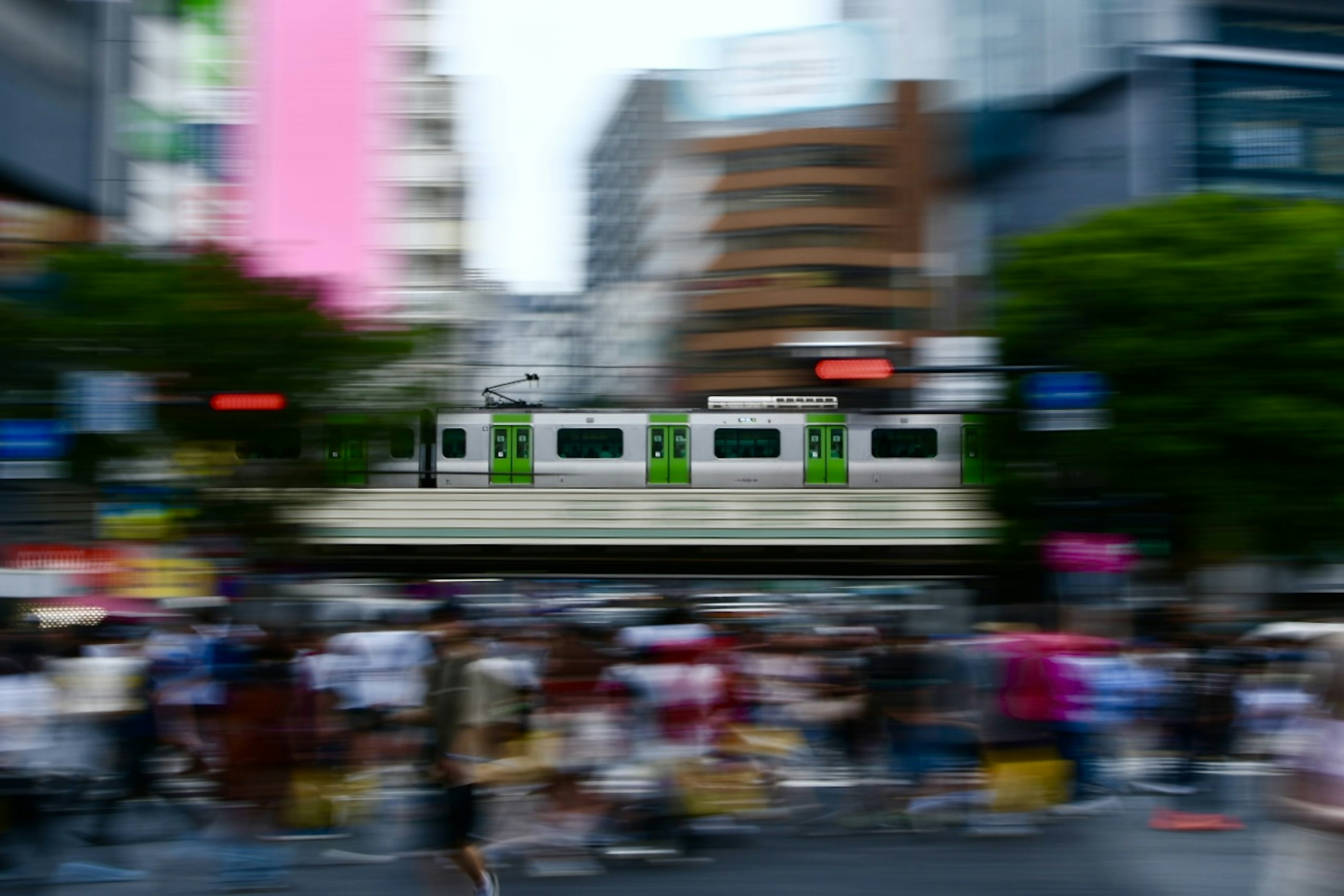 Blurred city scene with a green train passing and many people