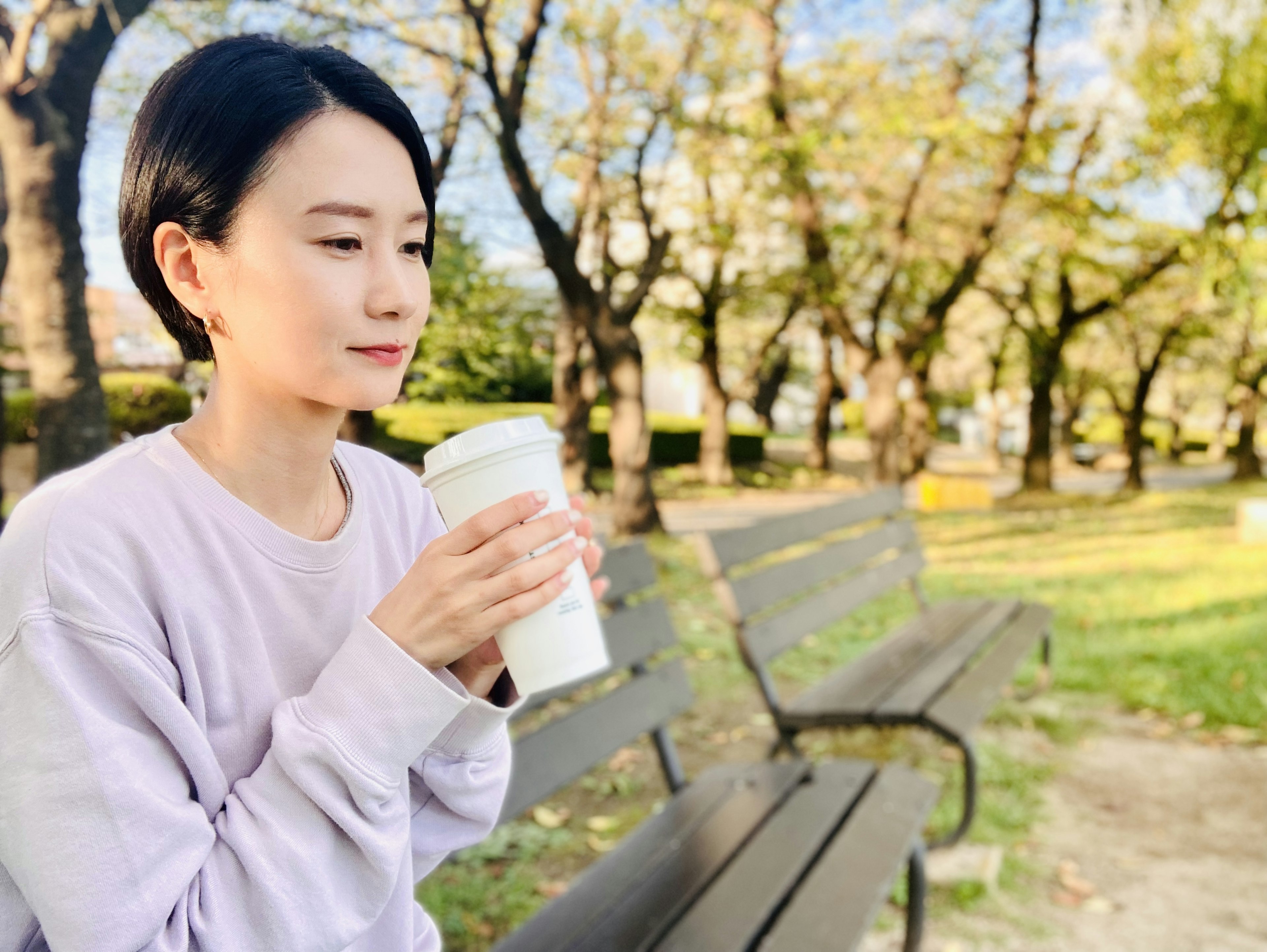 Mujer sentada en un banco del parque sosteniendo una taza de café