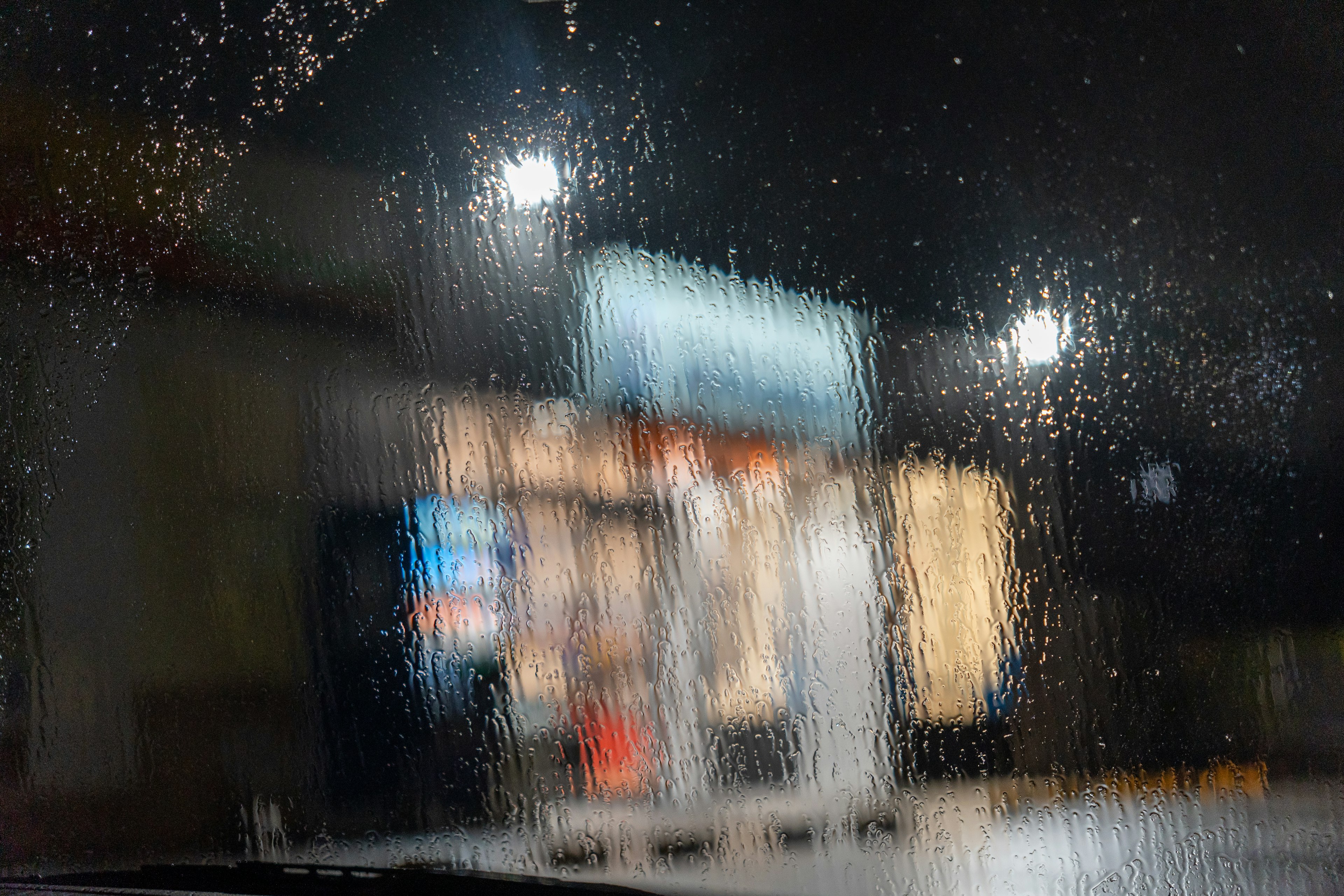 Blurry view of a restaurant exterior through rain on a car window at night