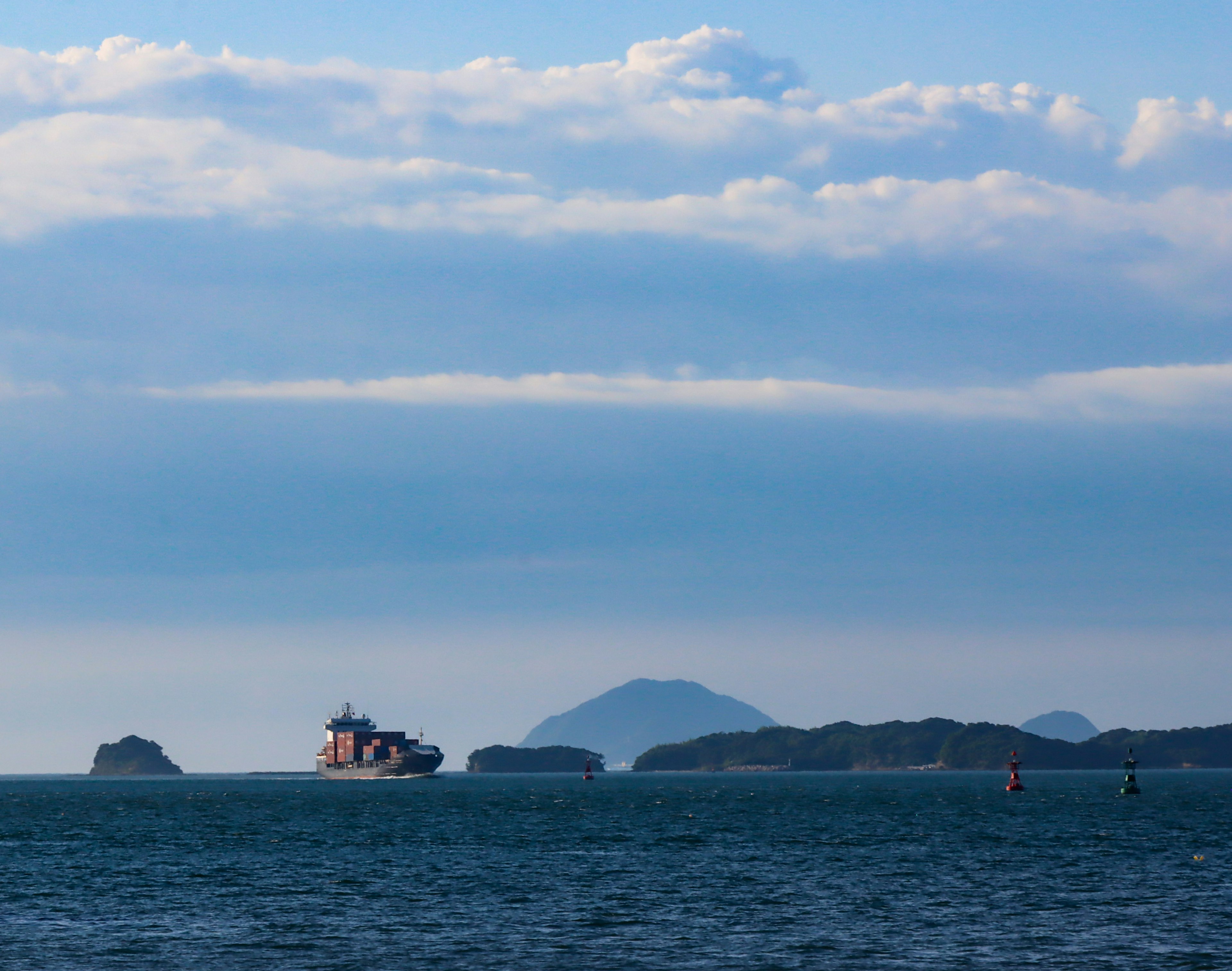 Kapal kargo di atas air biru dengan pulau-pulau jauh dan awan