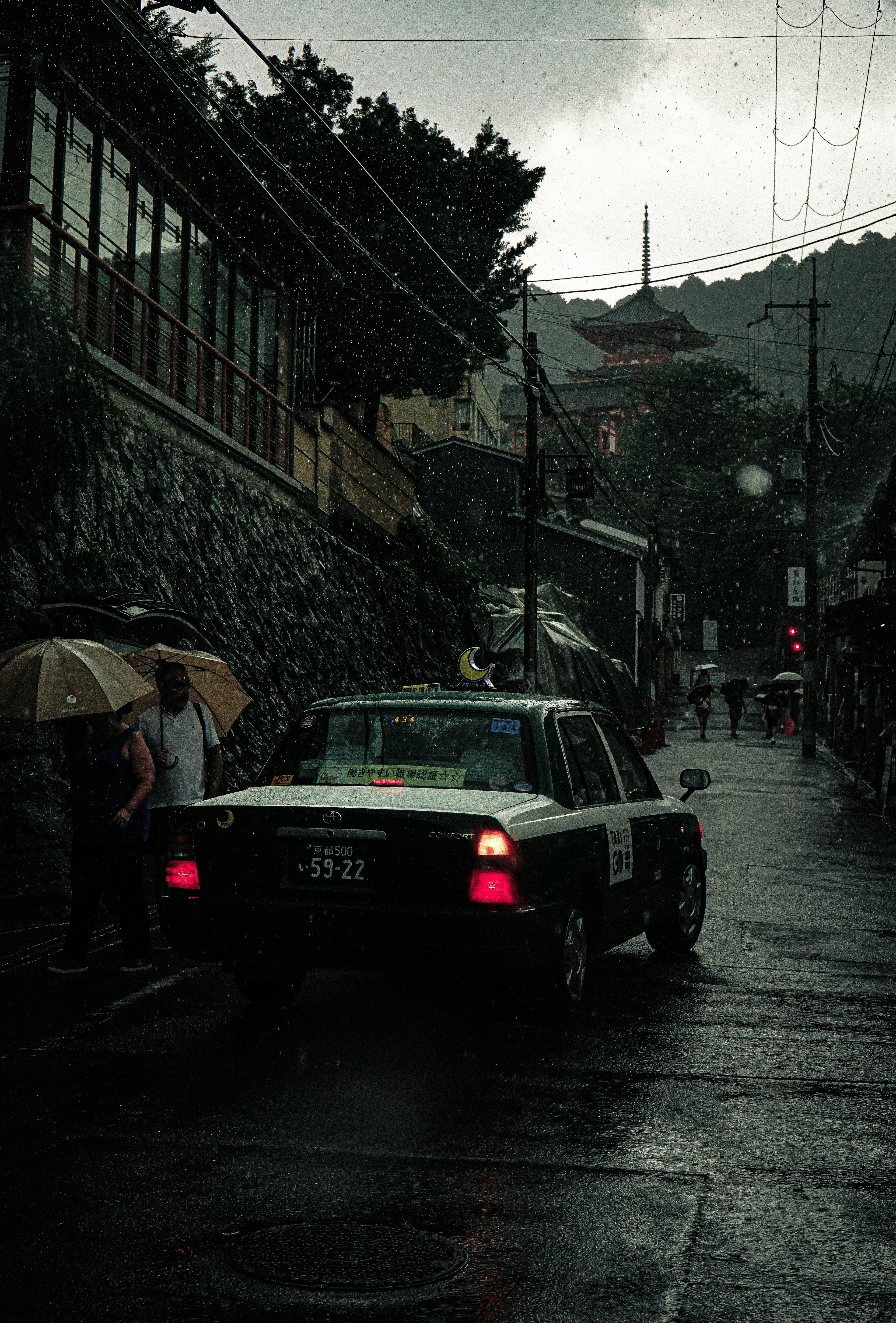 雨の中を走るタクシーと傘をさした人々の情景