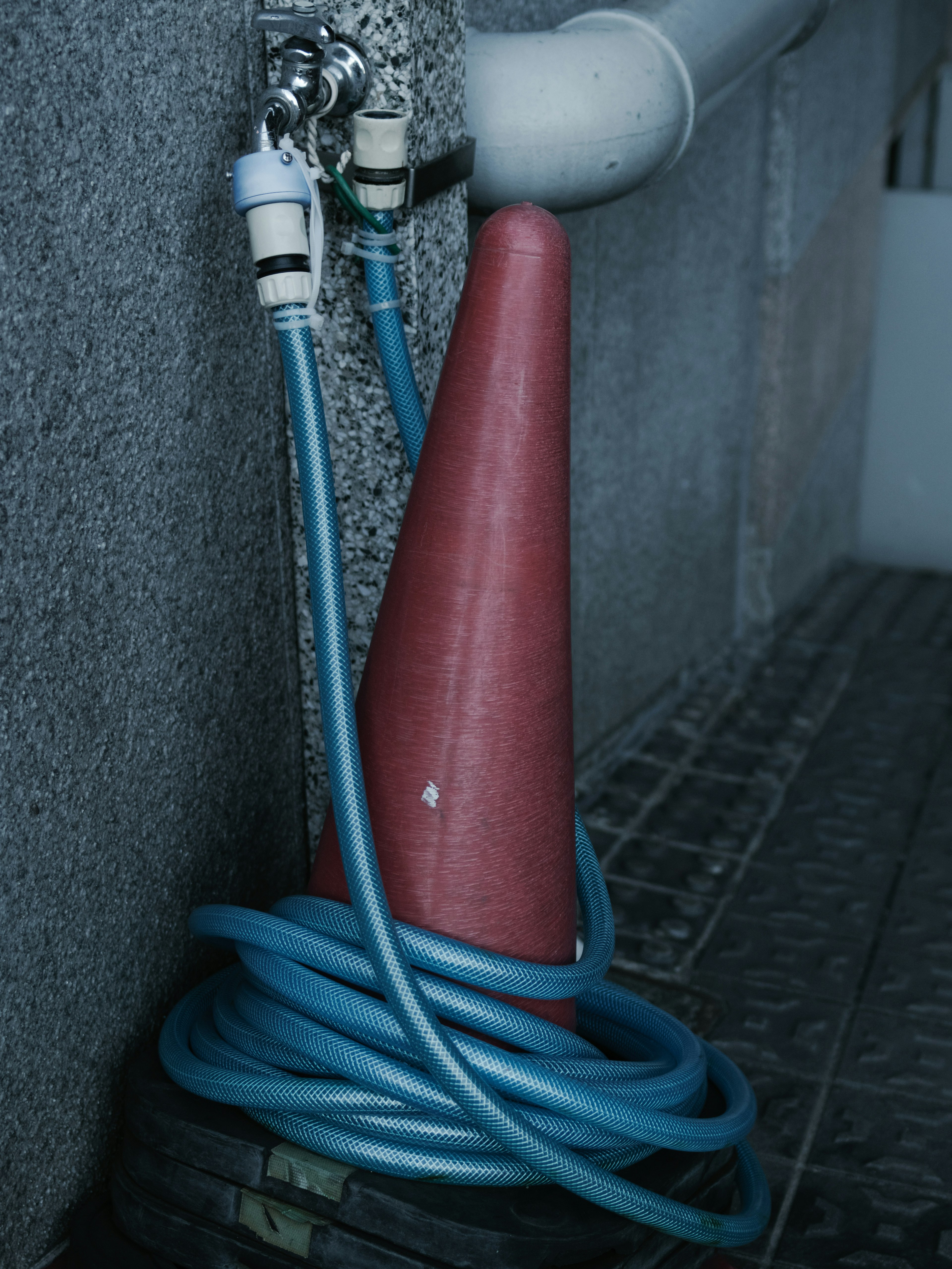 Cono rojo con mangueras azules apoyado contra una pared