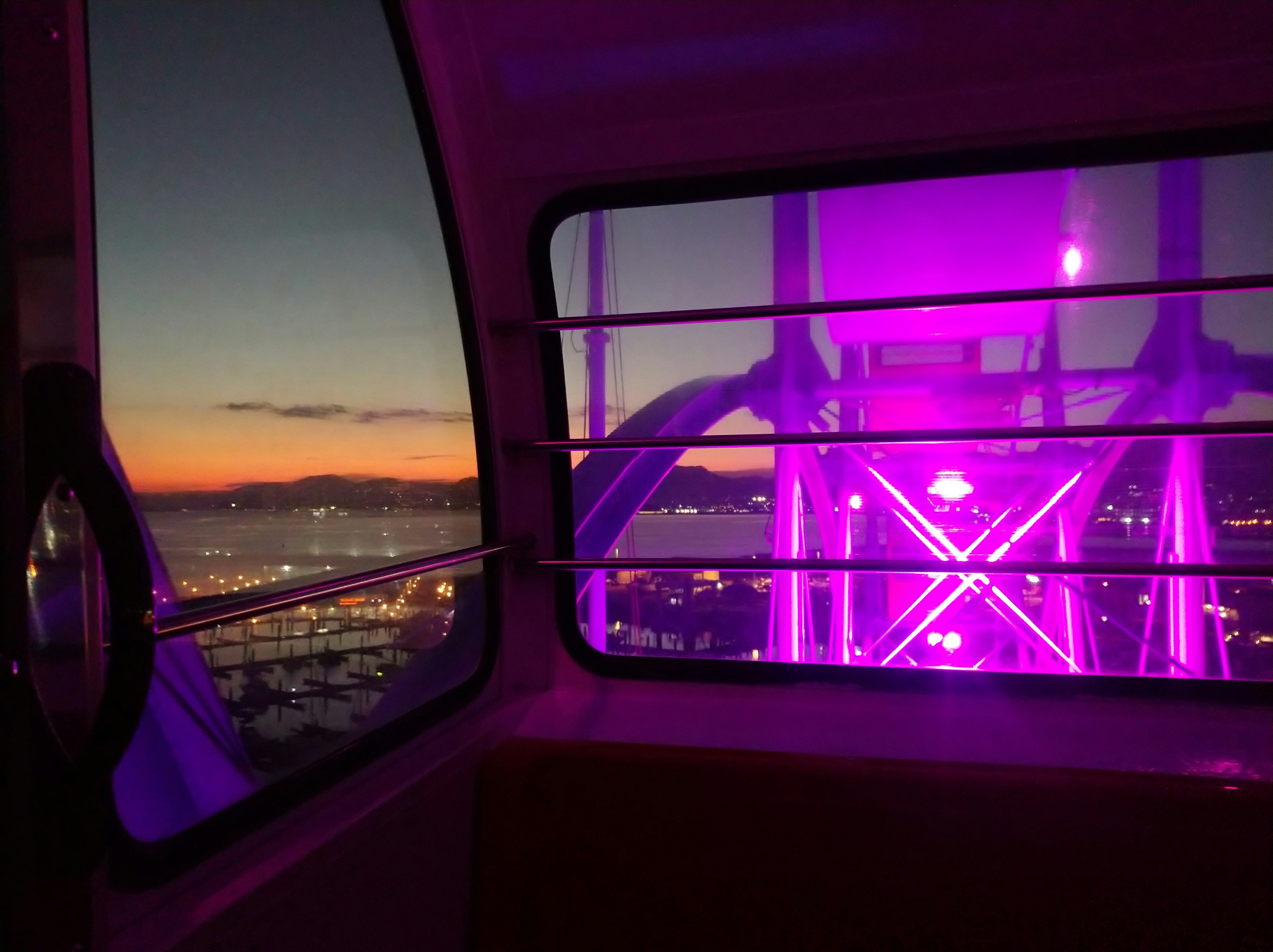 View from inside a gondola showcasing a purple-lit Ferris wheel at sunset