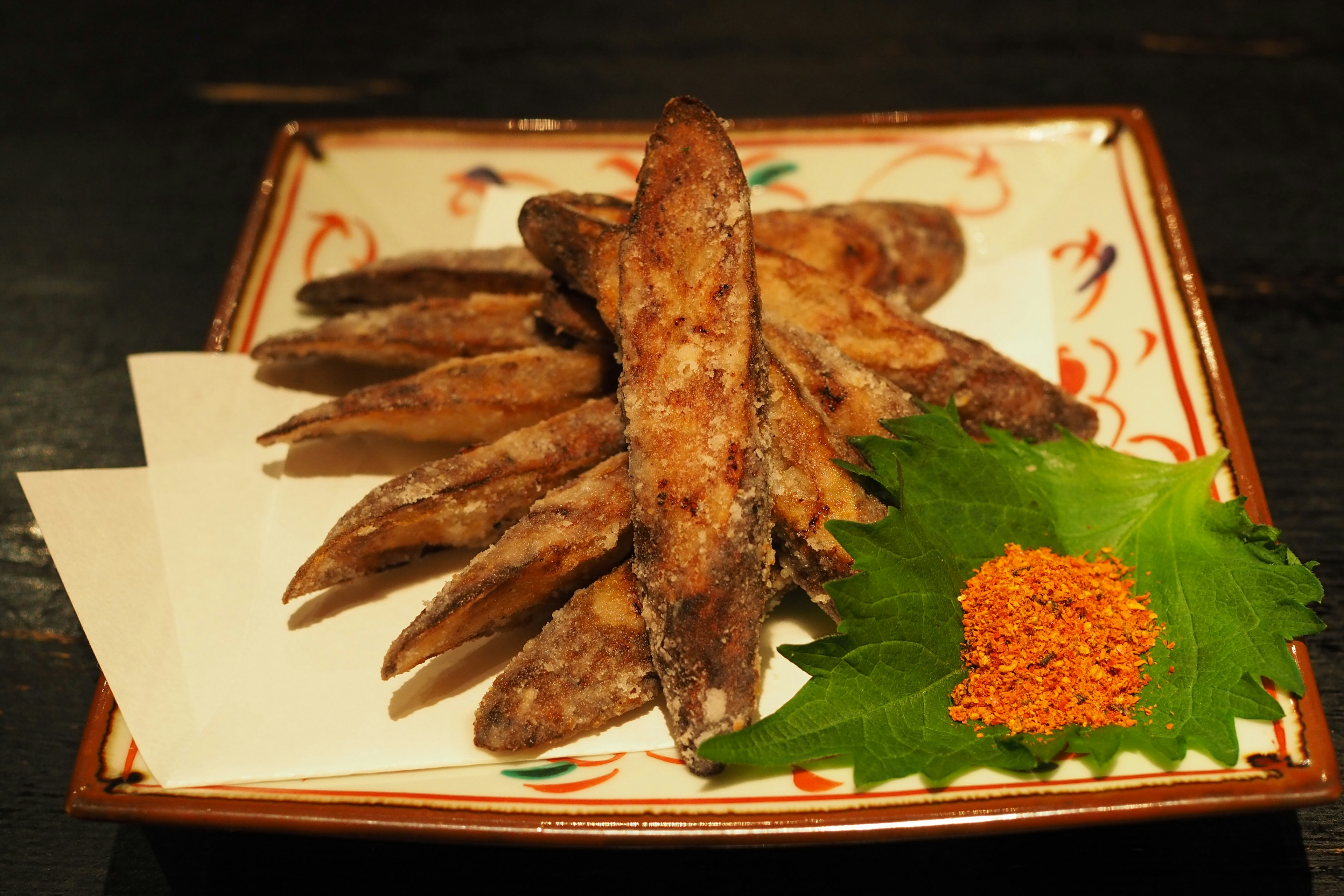 Fried fish fillets arranged on a decorative plate with green leaf and orange sauce