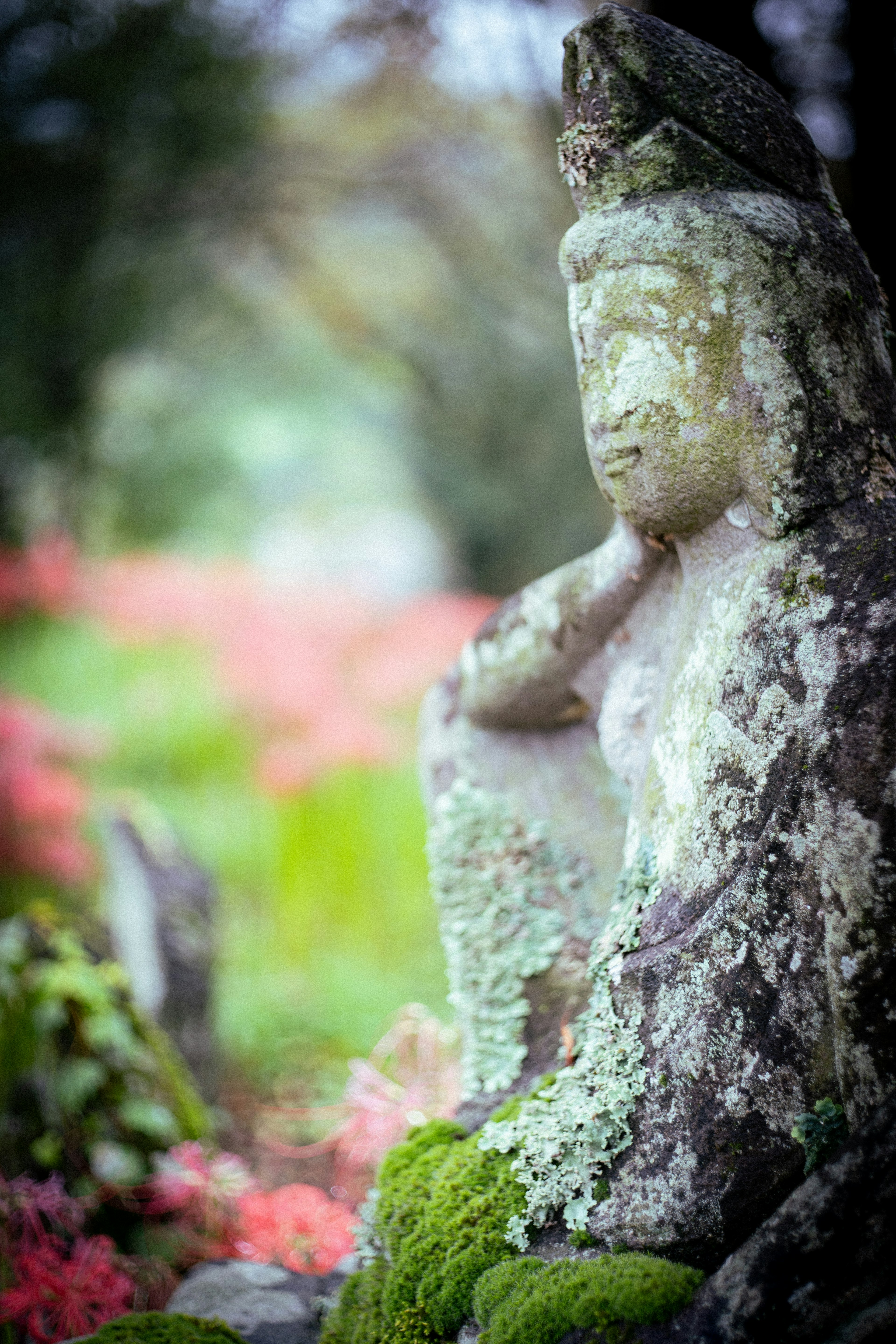 緑の苔と花に囲まれた古い仏像のクローズアップ