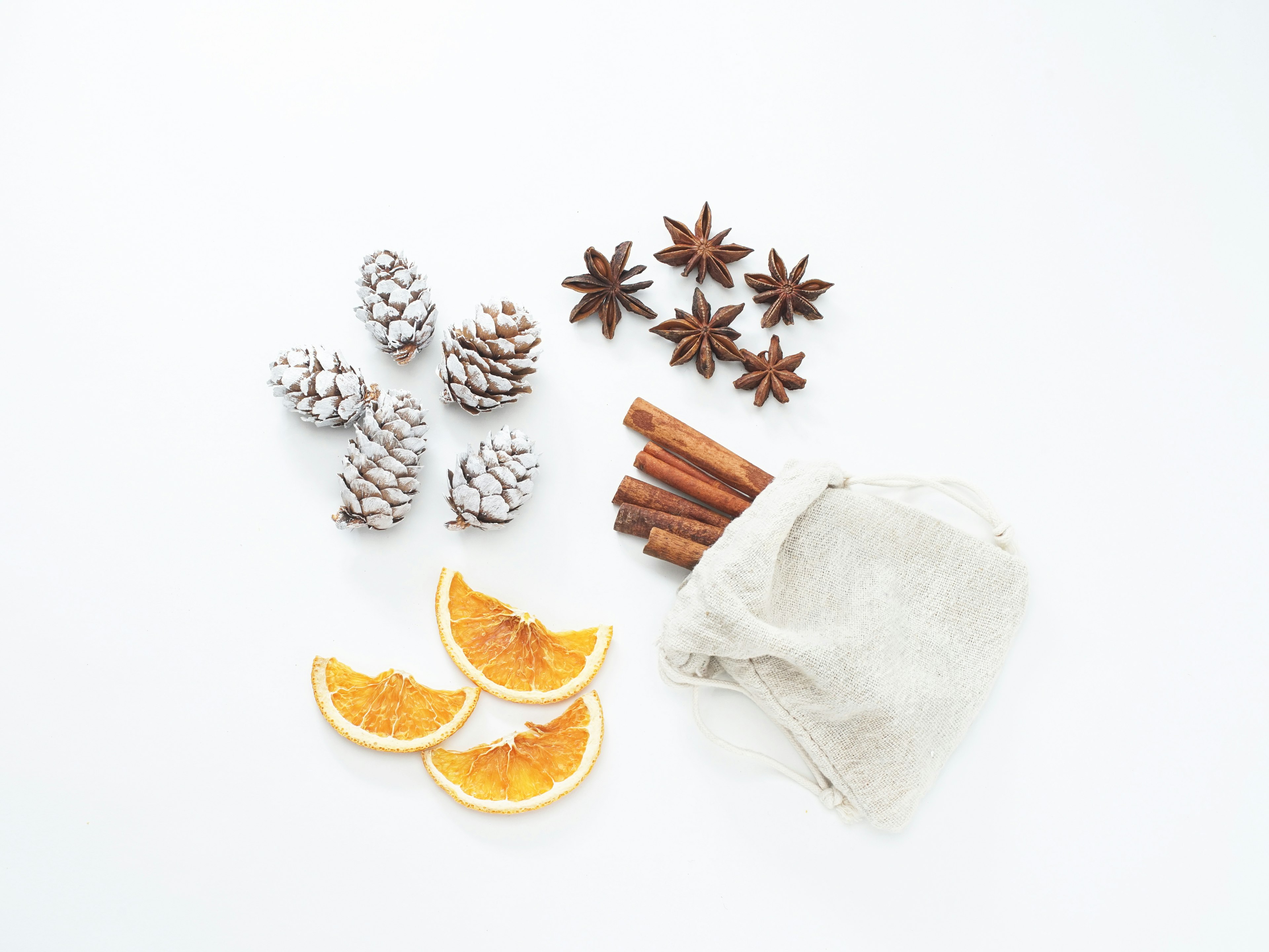 Piñas de pino, palitos de canela, anís estrellado y rodajas de naranja seca dispuestas sobre un fondo blanco