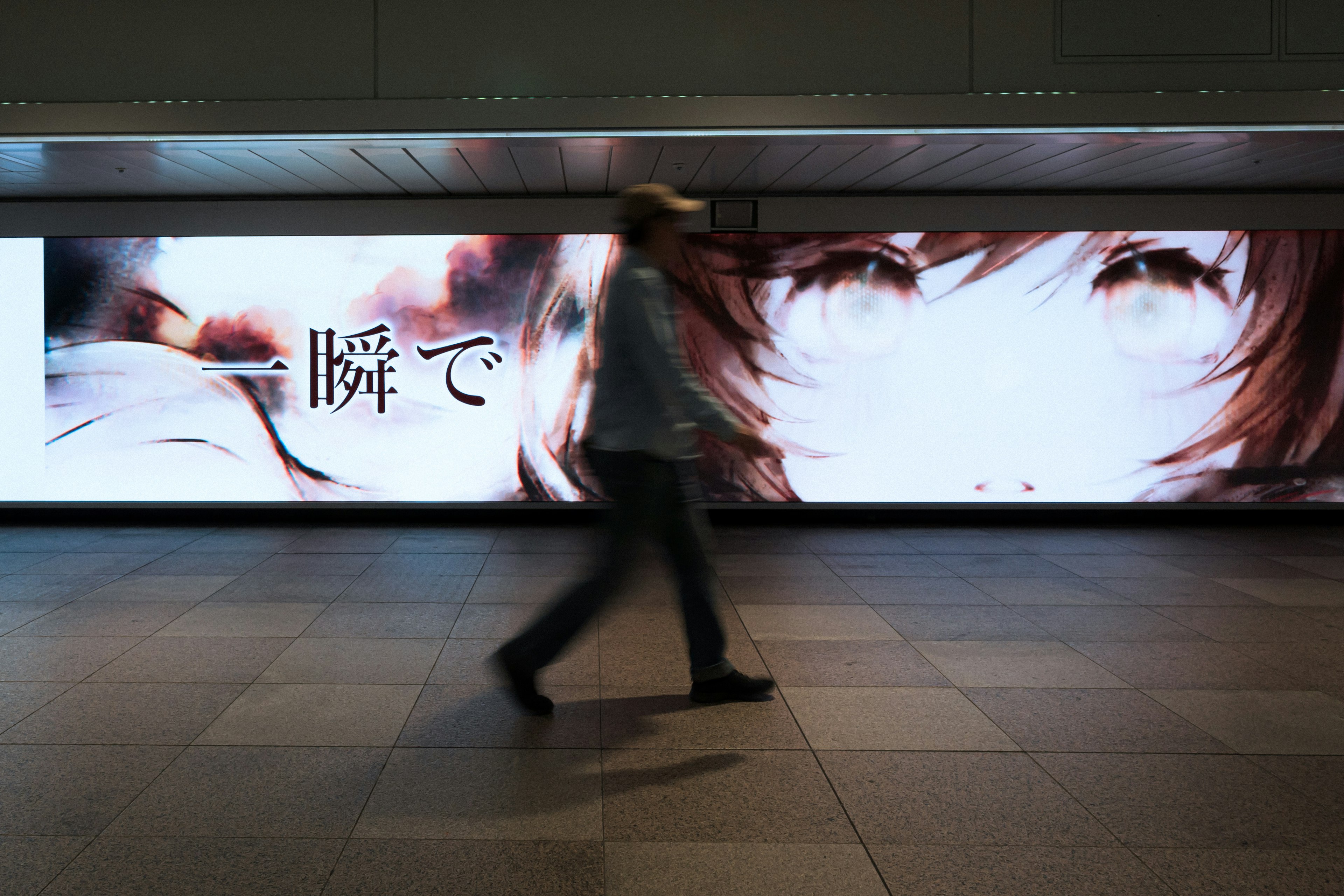 Une personne marchant devant un grand affichage artistique dans une gare