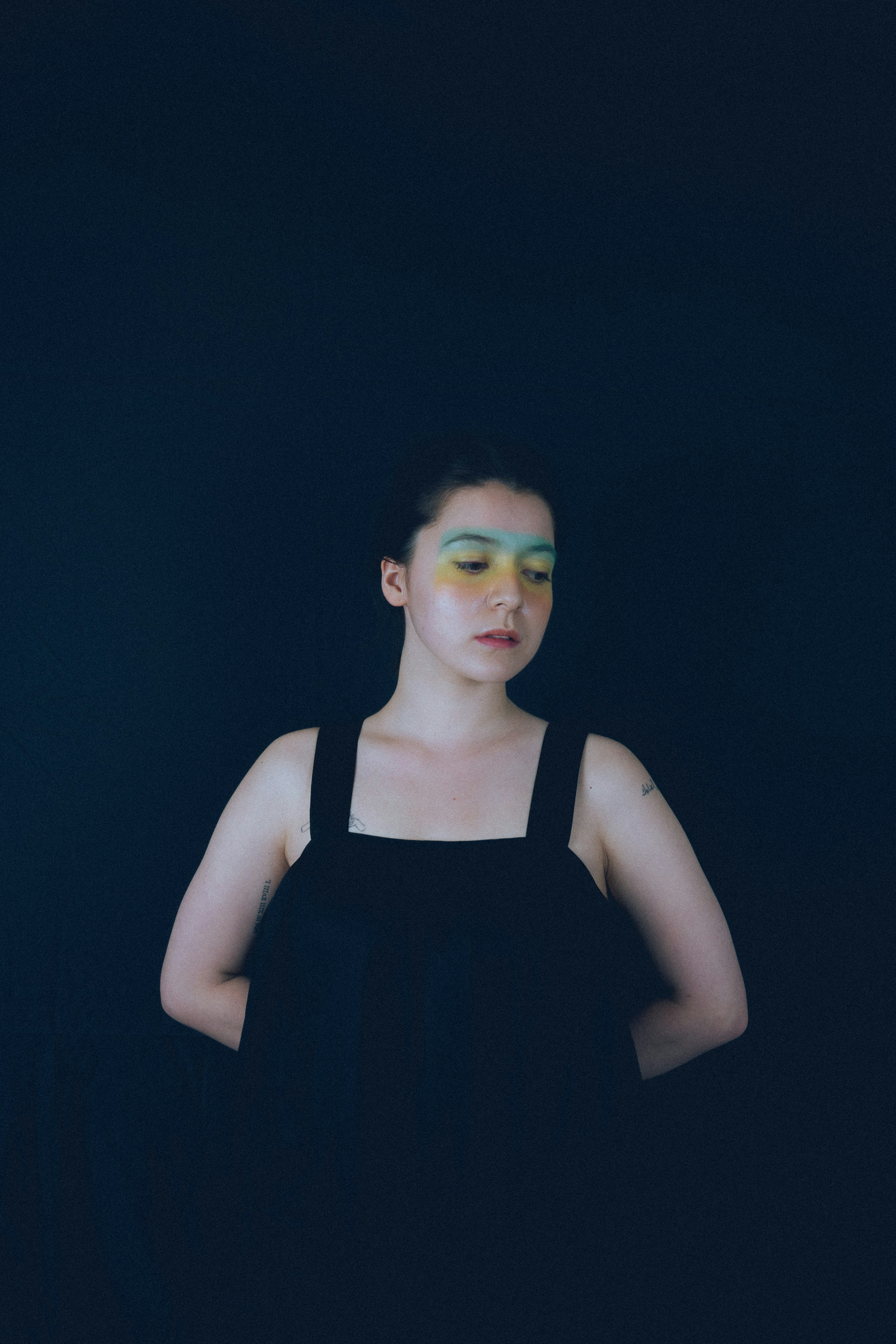 Portrait of a woman against a dark background featuring green eye makeup and a black dress