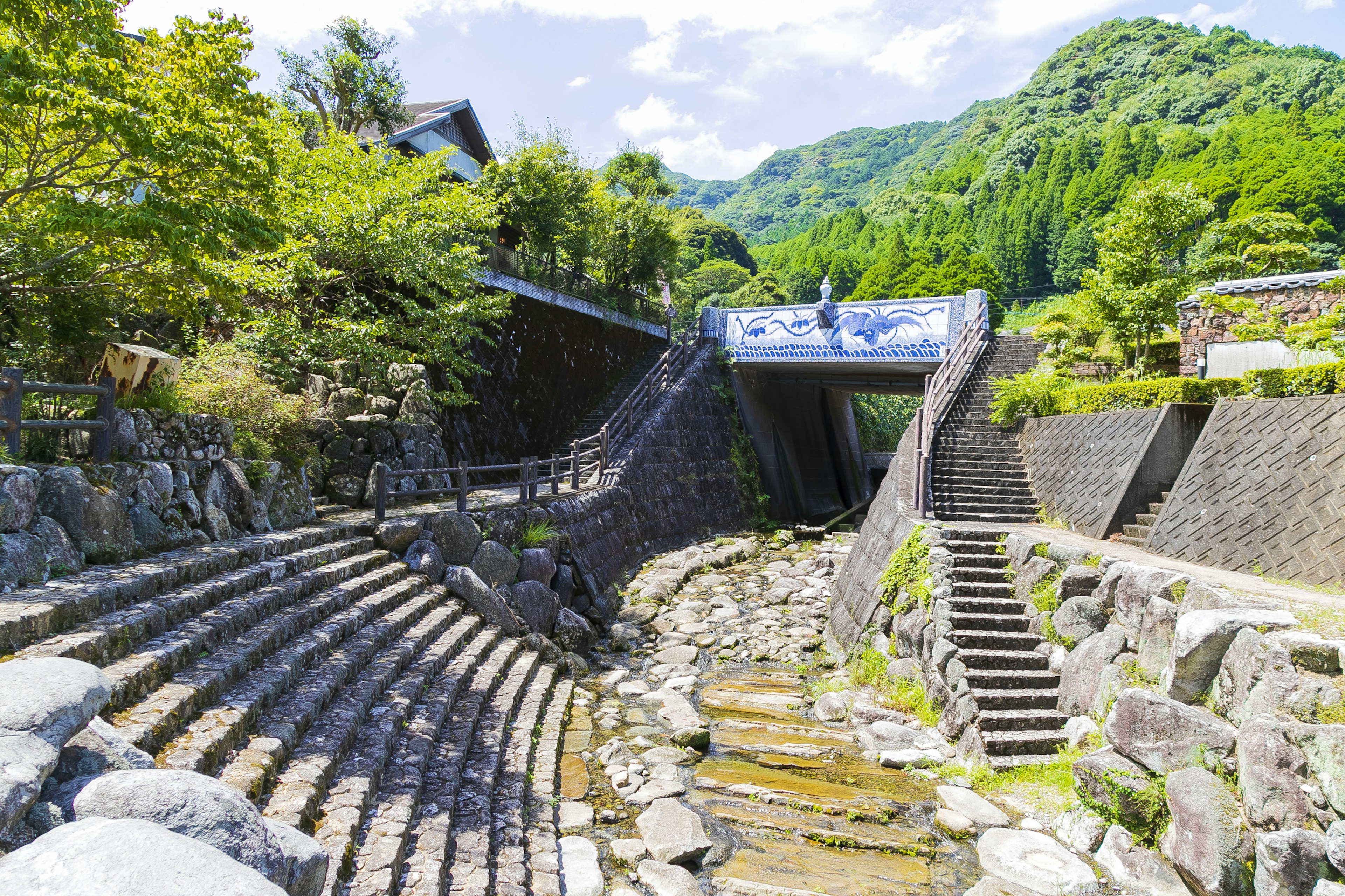 Vista escénica junto al río rodeada de vegetación exuberante con escaleras de piedra y un puente