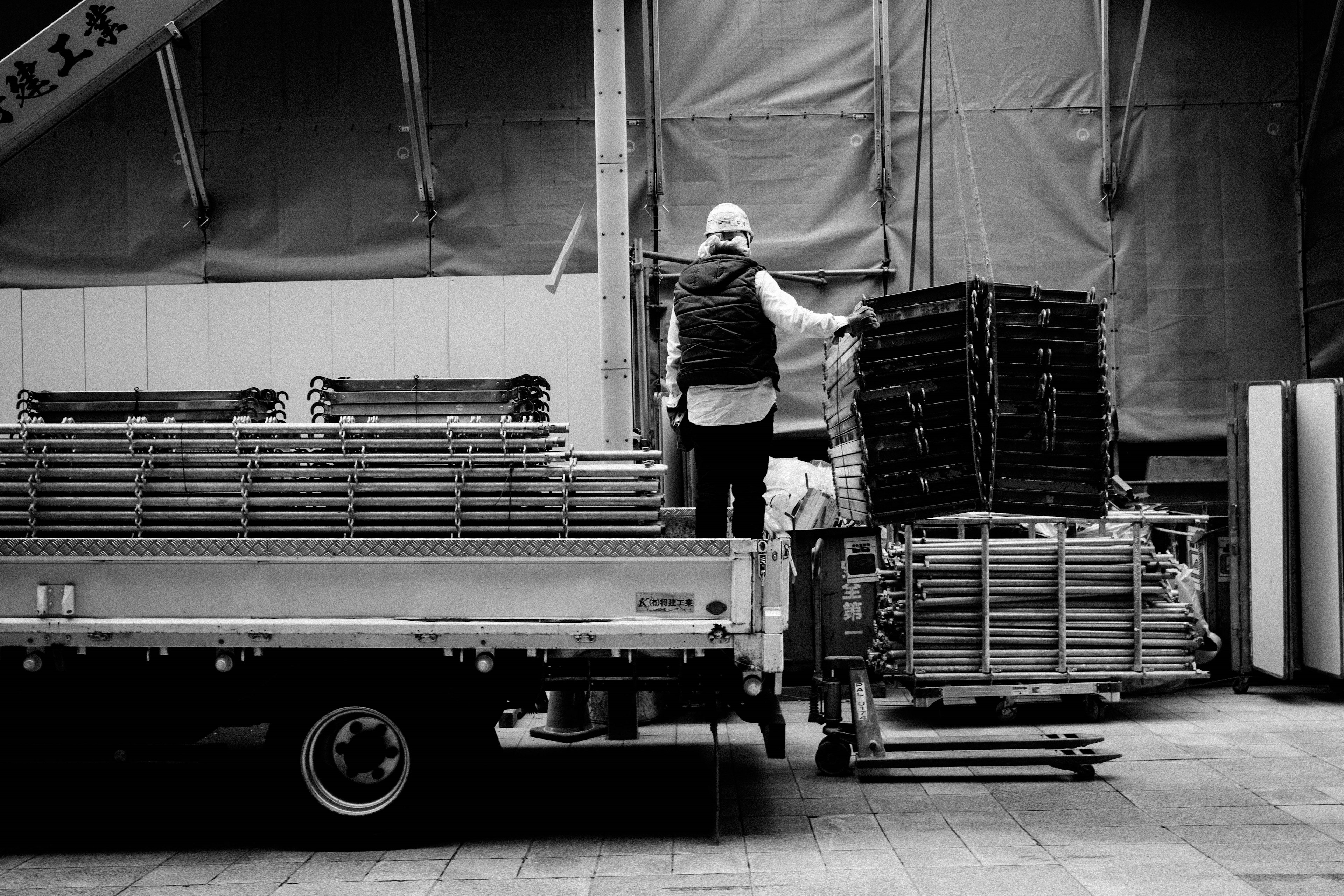 Schwarzweißfoto eines Arbeiters, der Paletten auf einen Lastwagen lädt