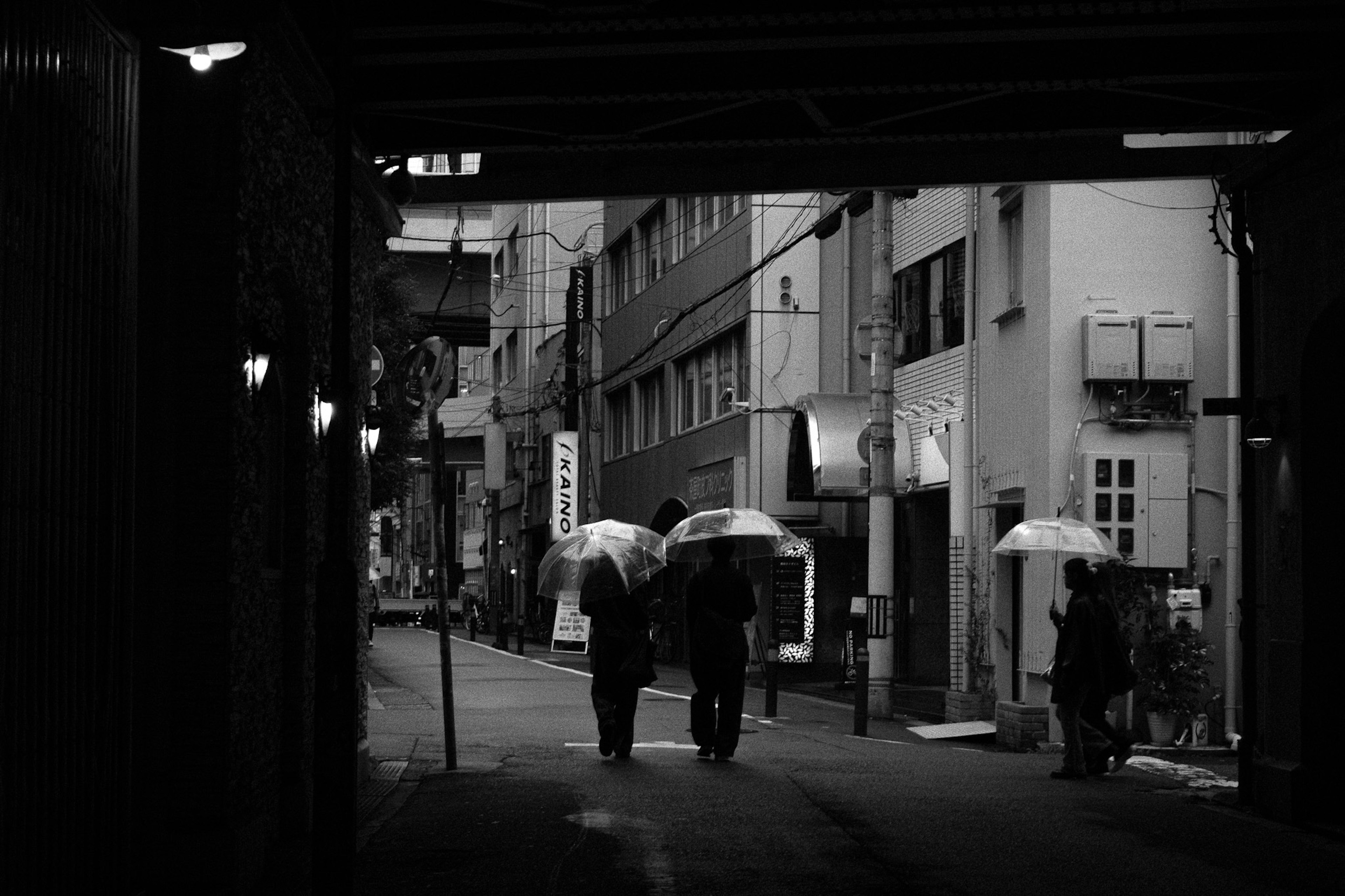 People walking with umbrellas in the rain on a city street in black and white