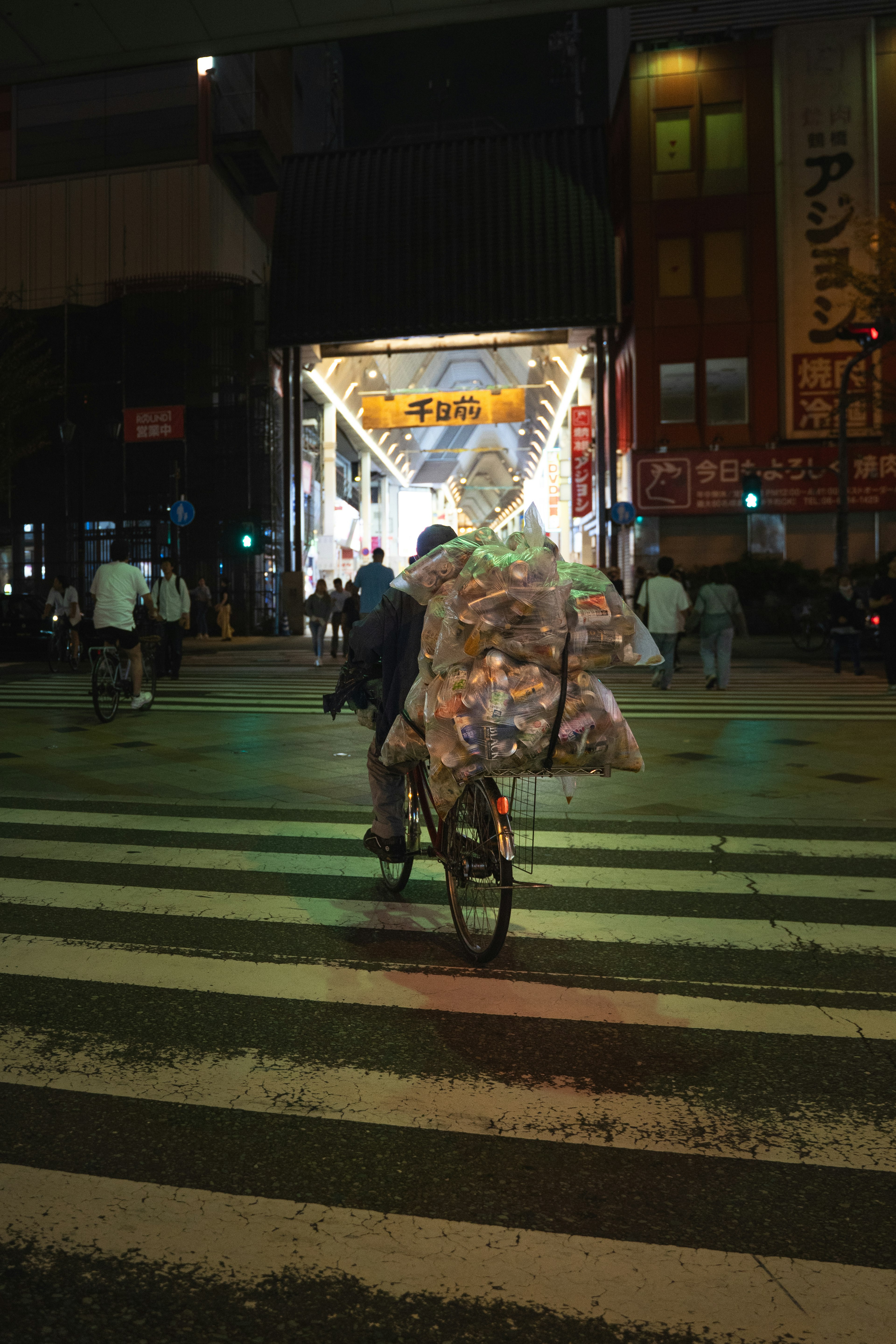 夜の交差点を渡る自転車の配達員 袋を積んだ自転車が歩行者を避けている