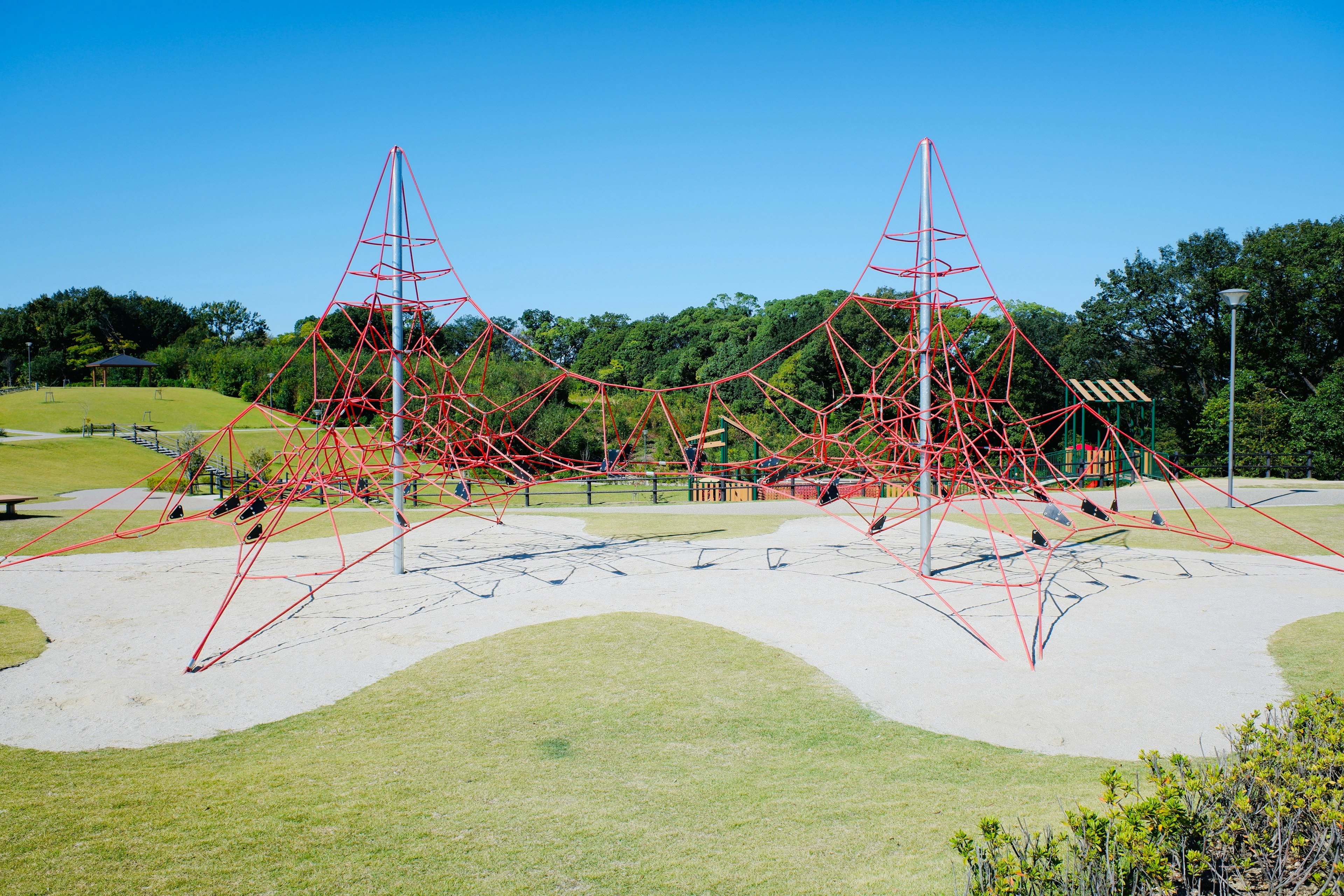 Spielplatz mit roten Kletterstrukturen umgeben von grünem Gras und blauem Himmel