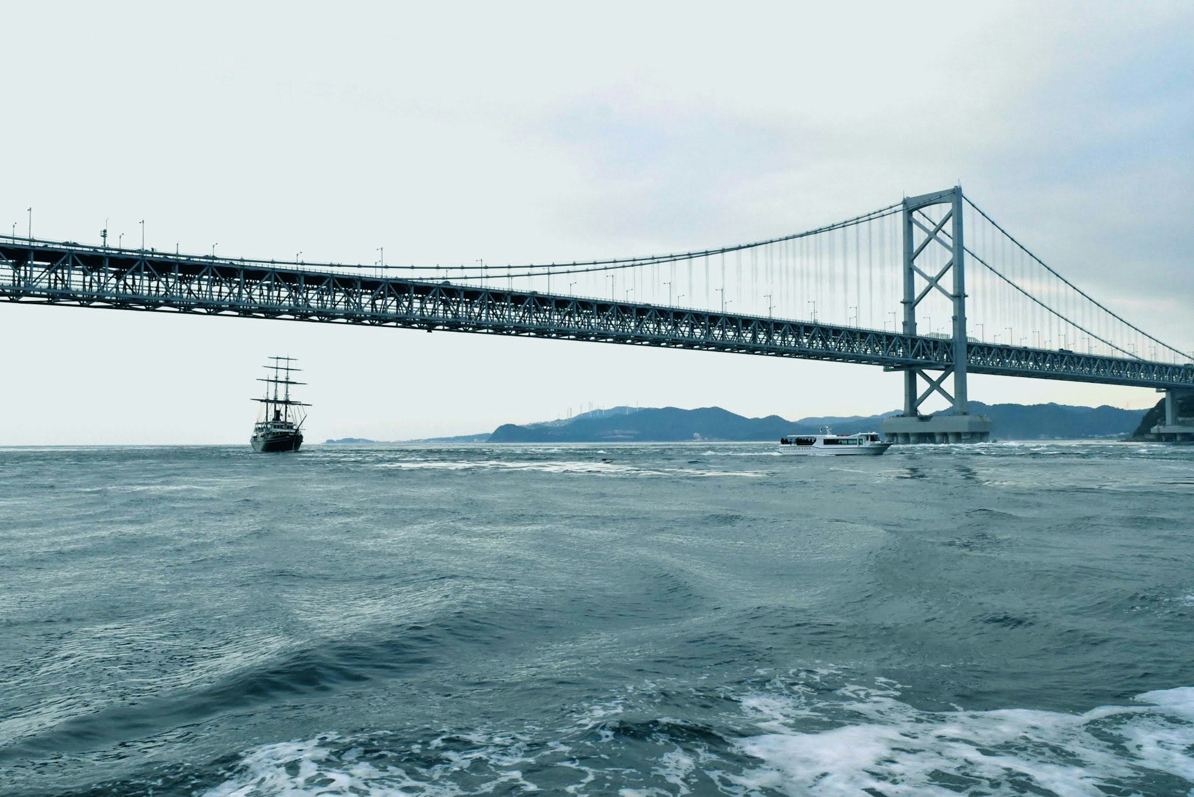 Gran puente sobre el mar con un barco de vela a la vista