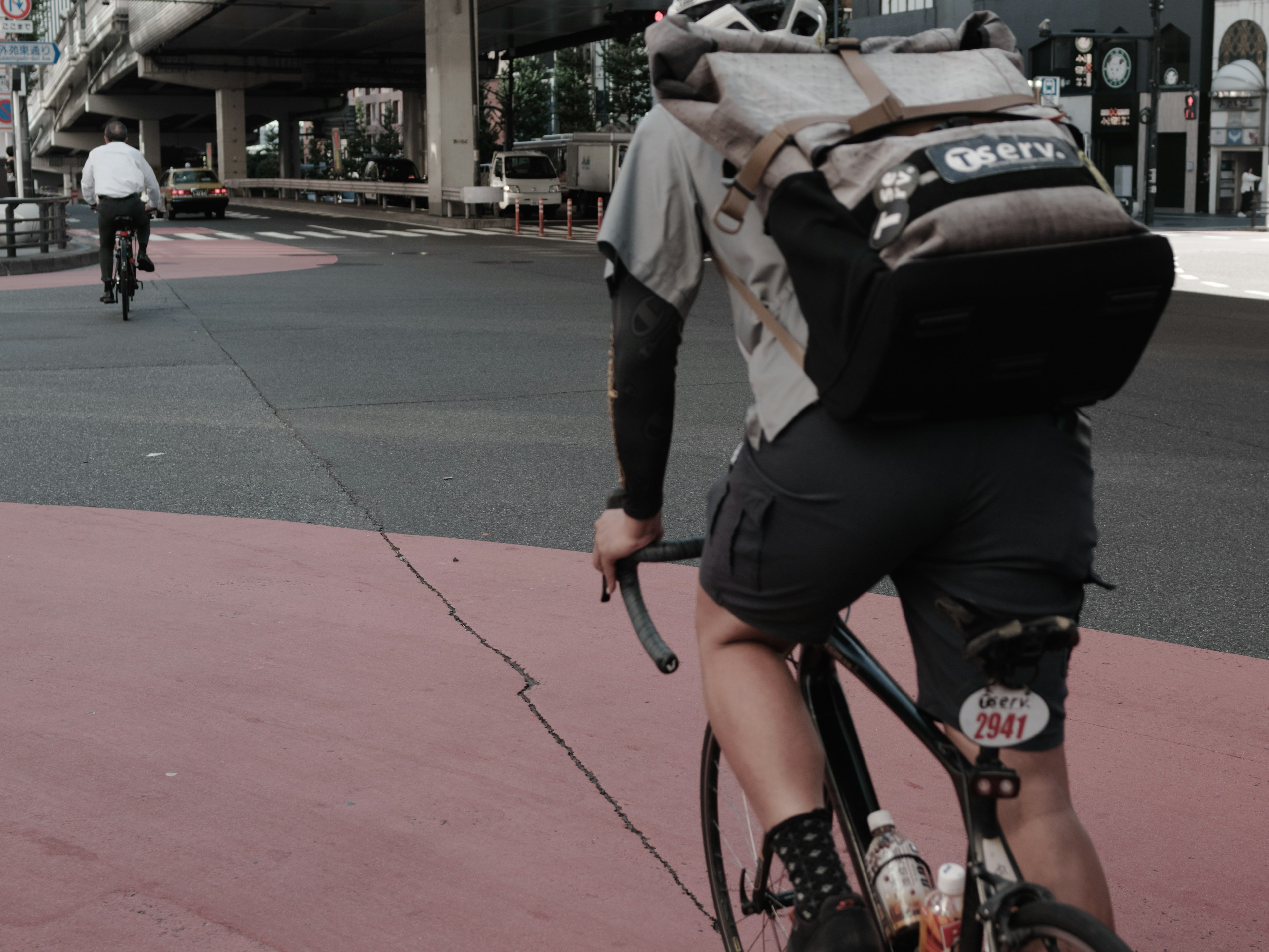 Repartidor en bicicleta con mochila en una carretera rosa