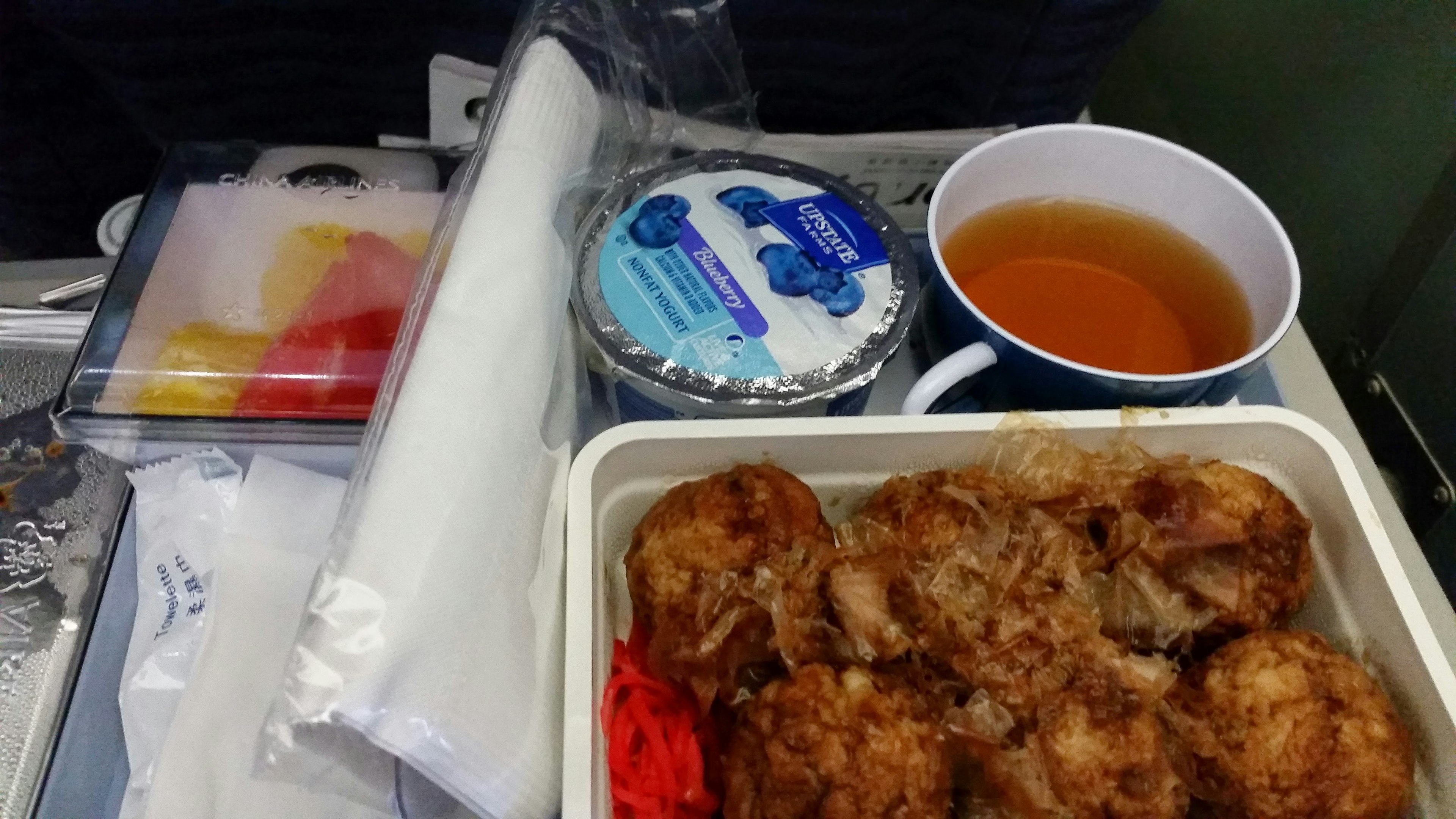 In-flight meal tray with fried chicken, dessert, and a cup of tea