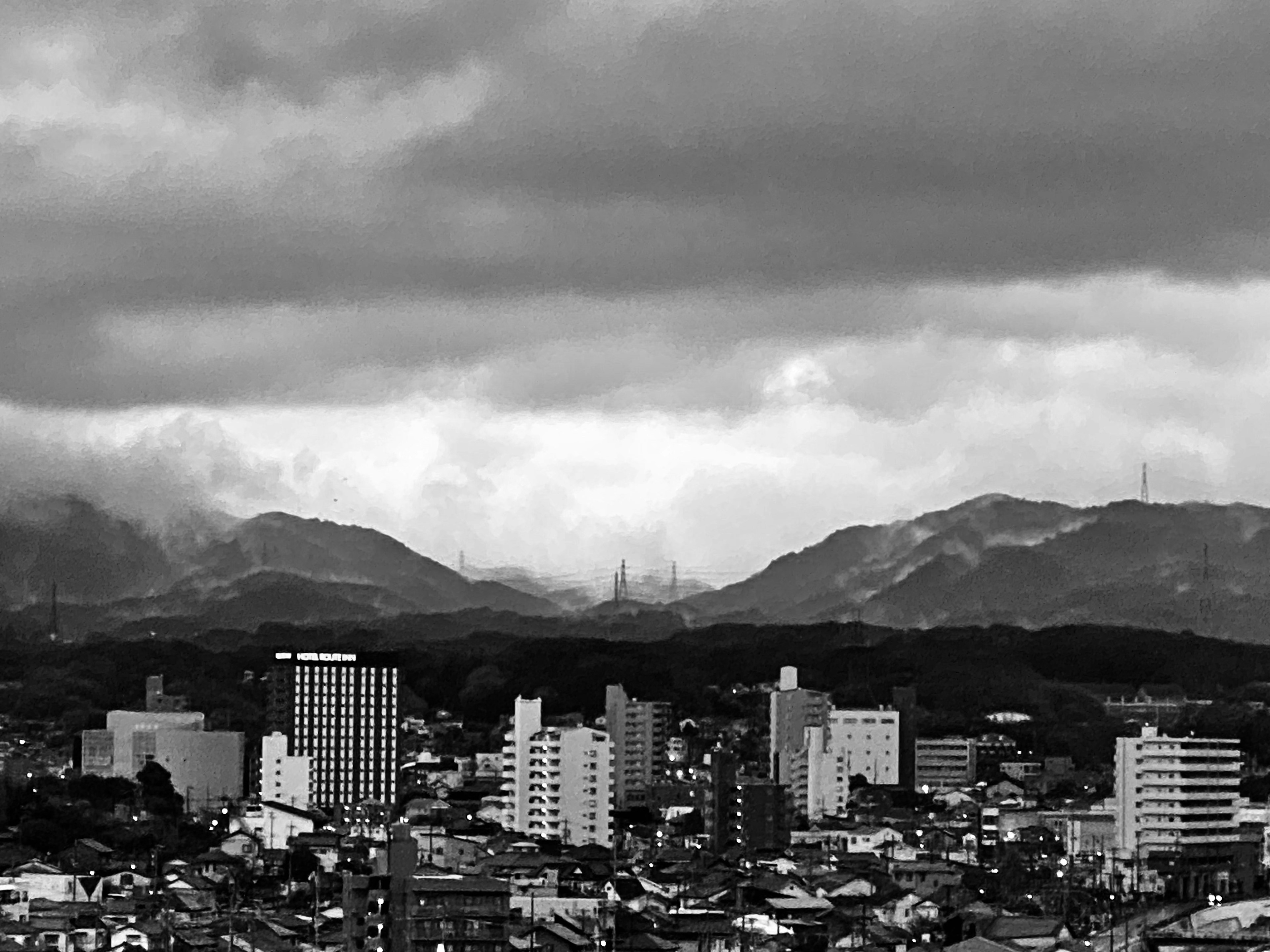 Paisaje urbano en blanco y negro con edificios altos y montañas al fondo