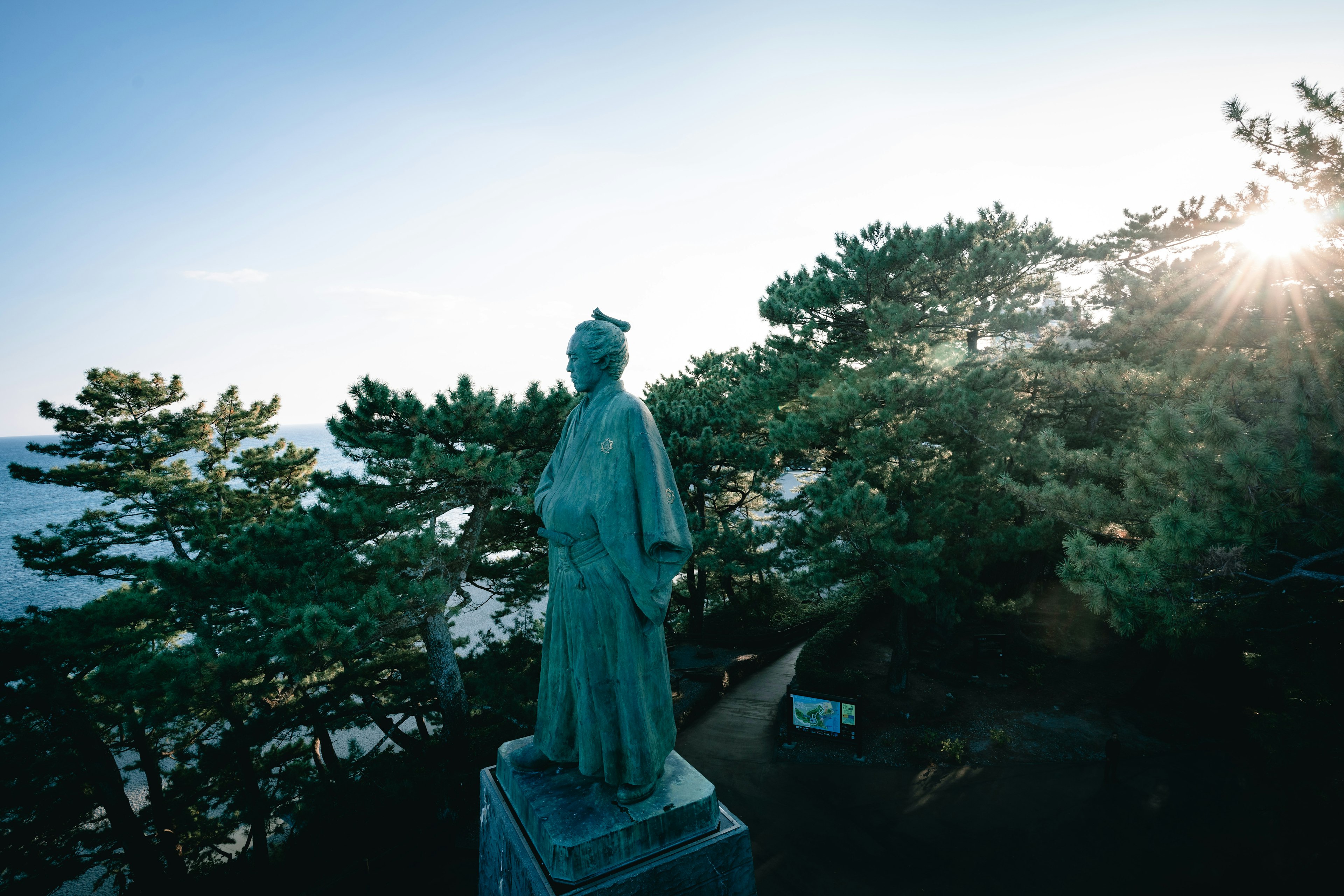 Estatua de bronce que contempla el mar con pinos