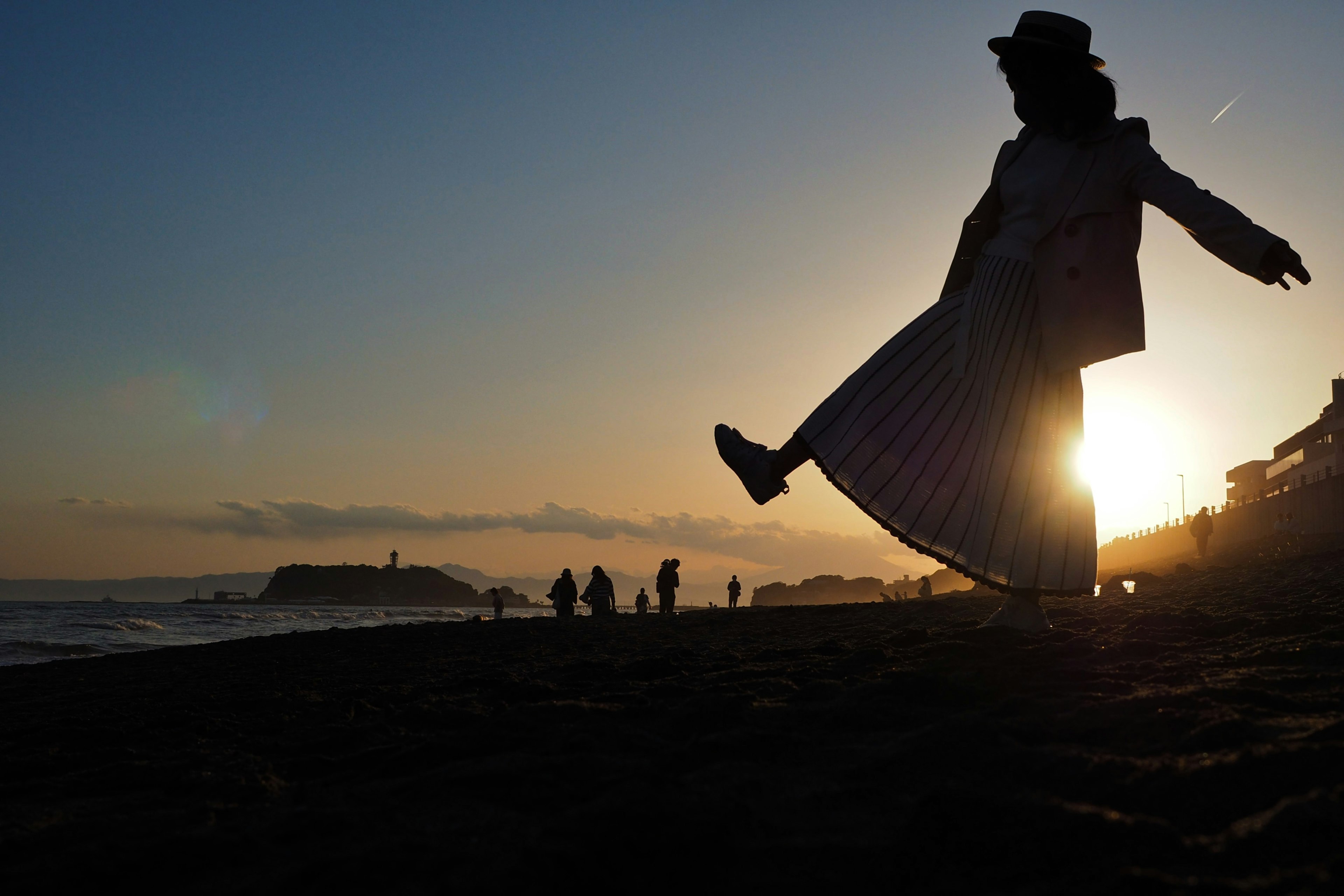 夕日を背にしたシルエットの人物がビーチを歩いている風景