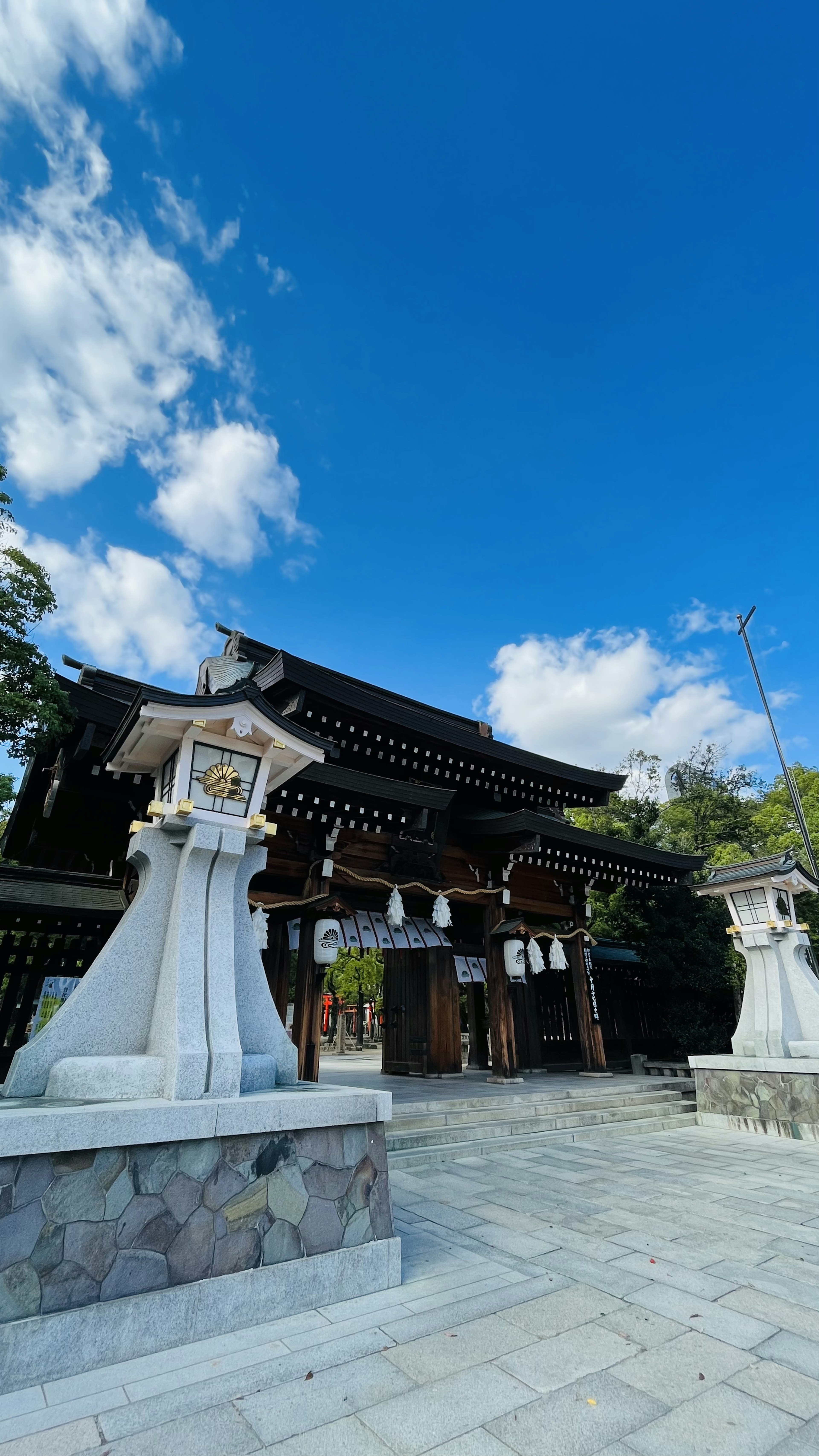 青空の下にある伝統的な神社の門と石灯篭