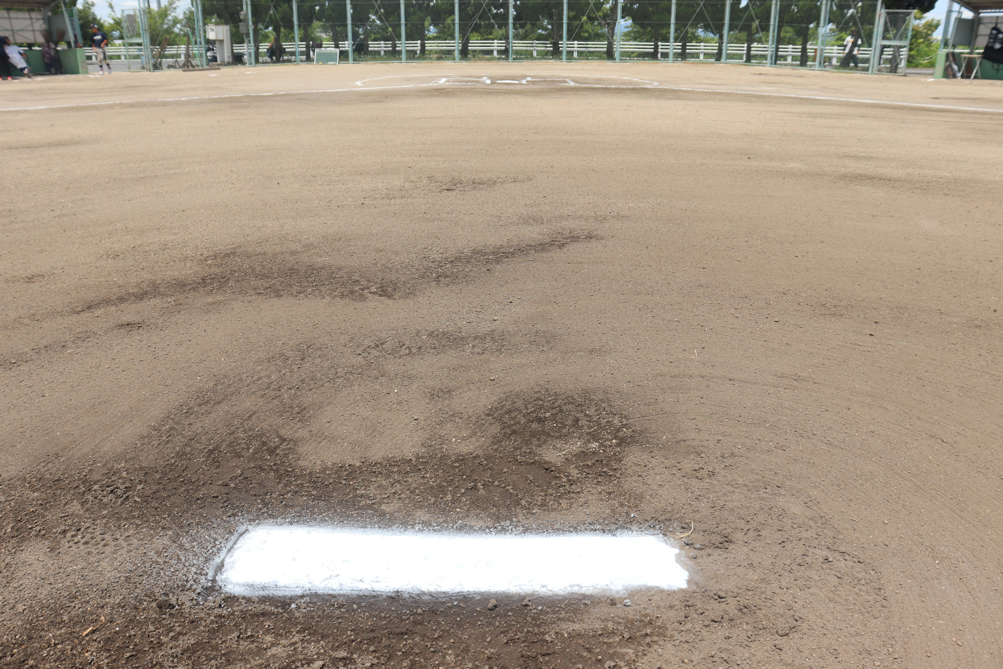 A baseball field with a diamond shape showing a white painted base in the center of the dirt area