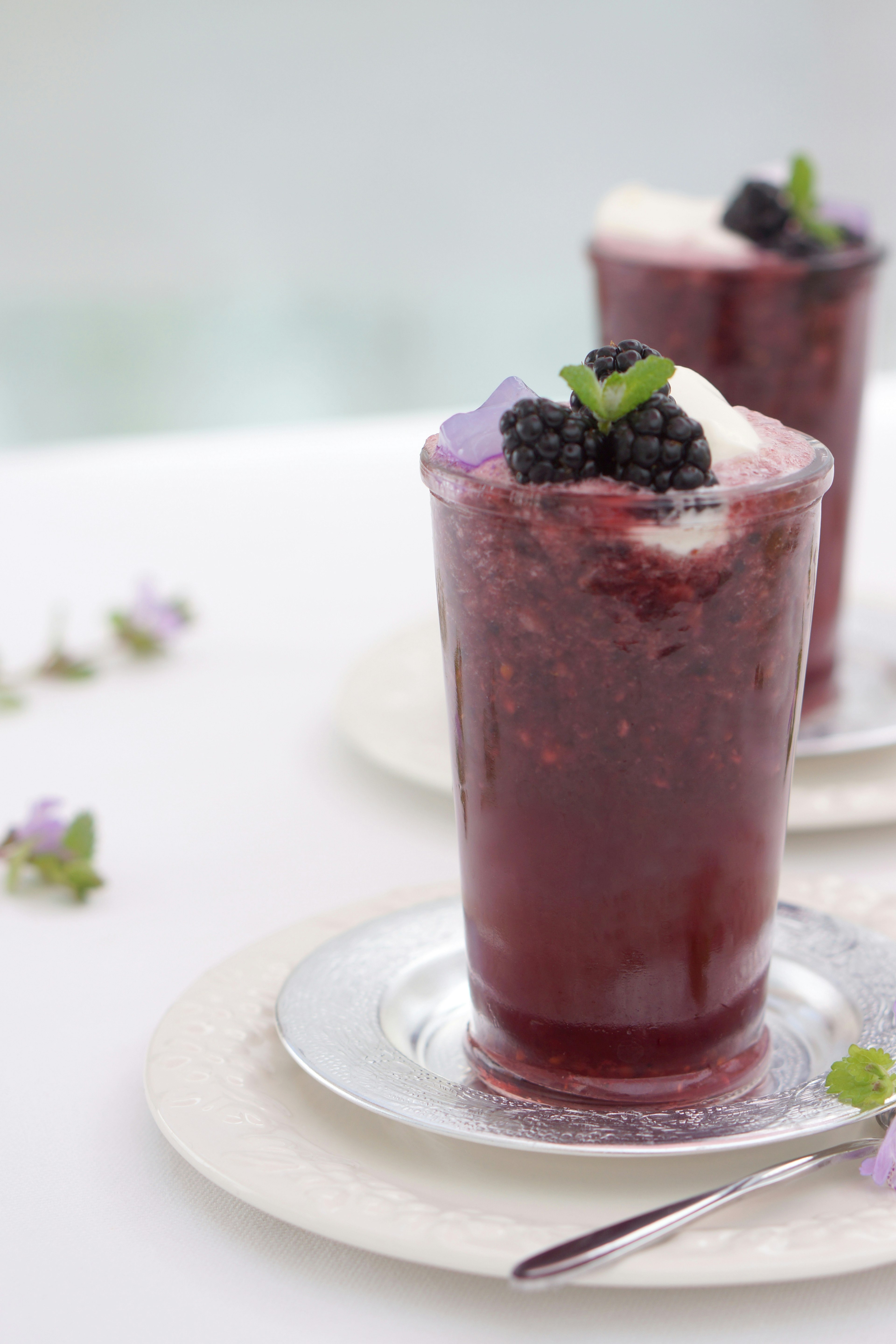 A glass of cold drink topped with blackberries and mint leaves