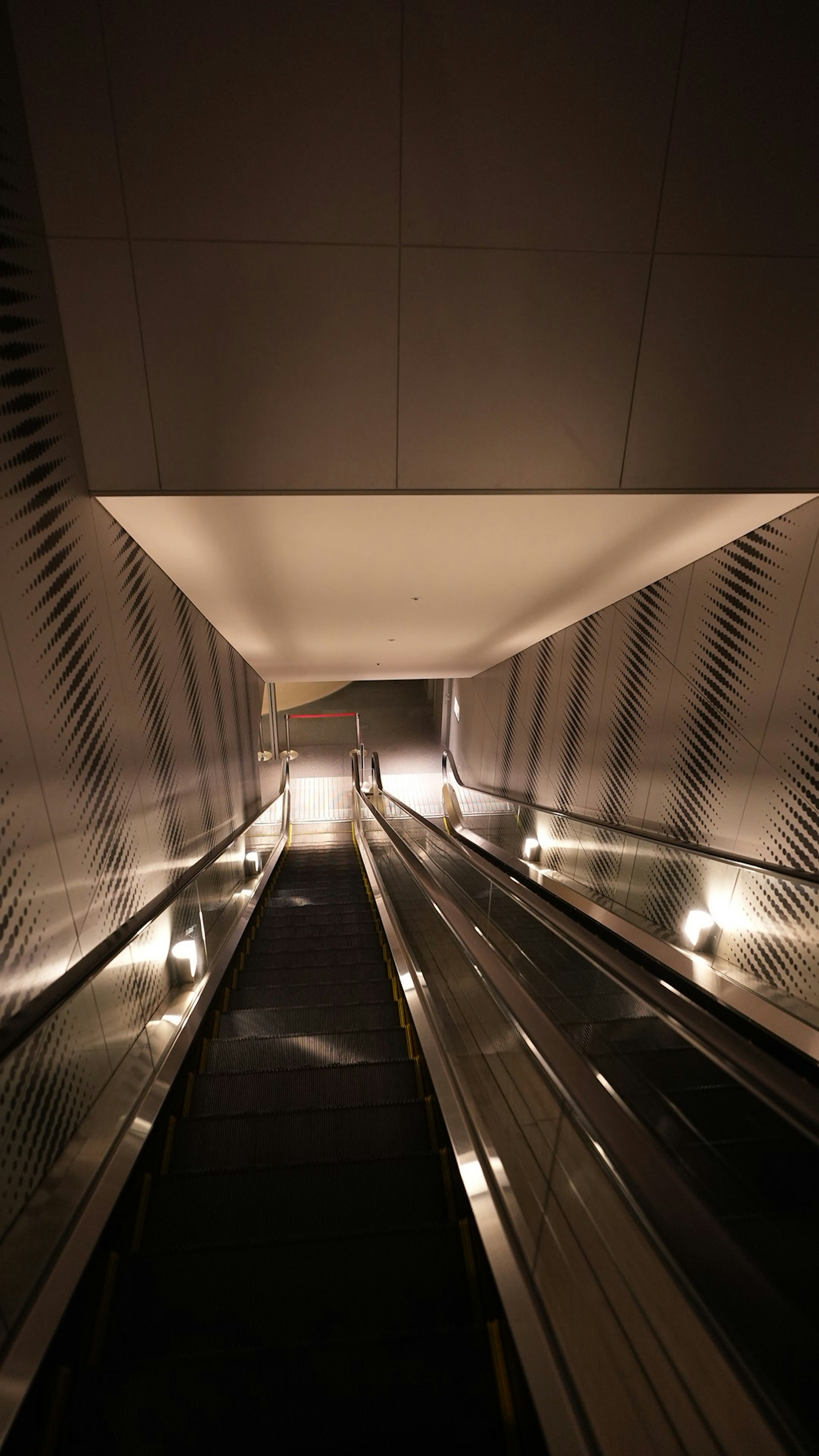 Blick auf eine Rolltreppe in einem schwach beleuchteten Korridor mit reflektierenden Oberflächen