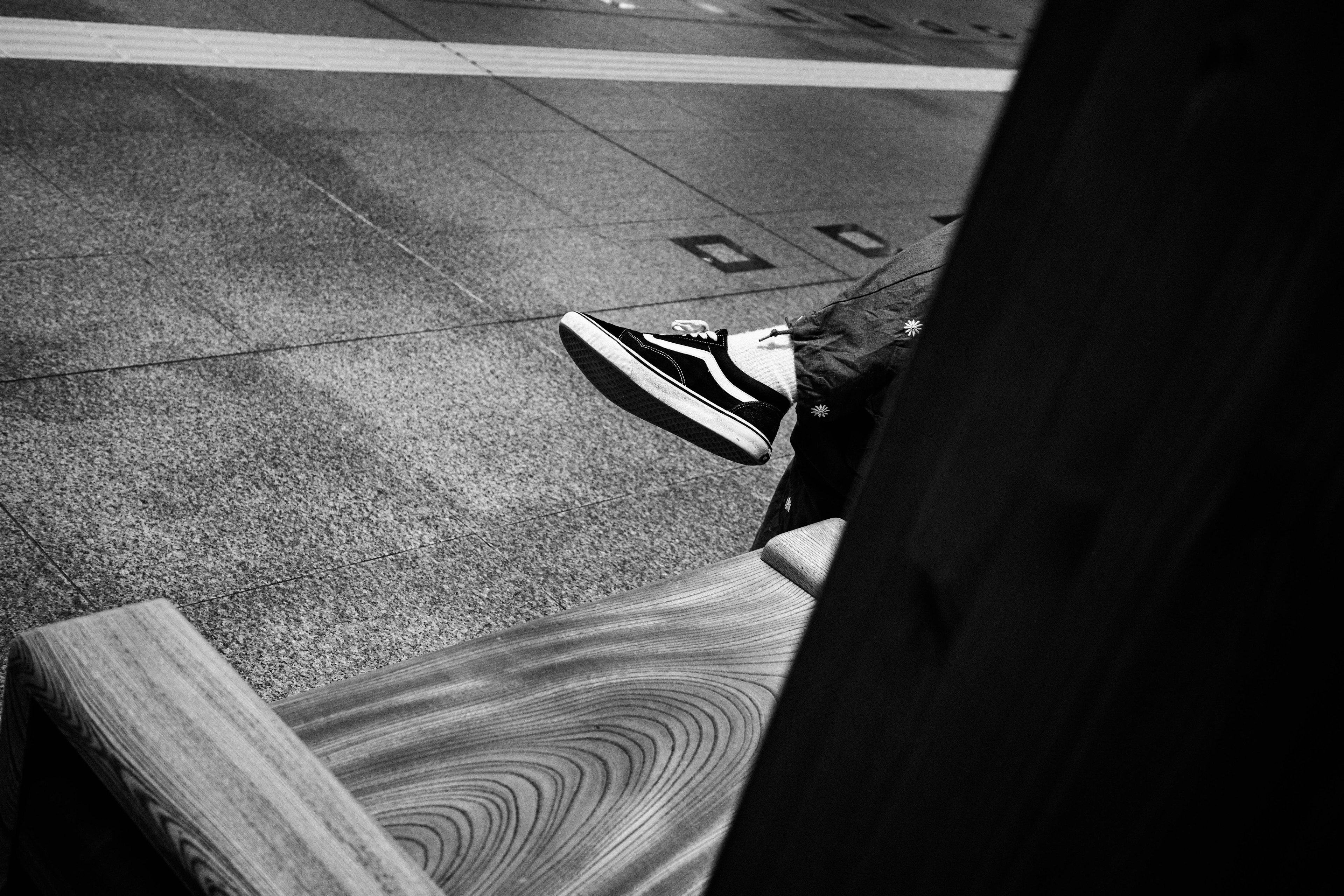 Black and white shoes resting on the ground part of a bench visible