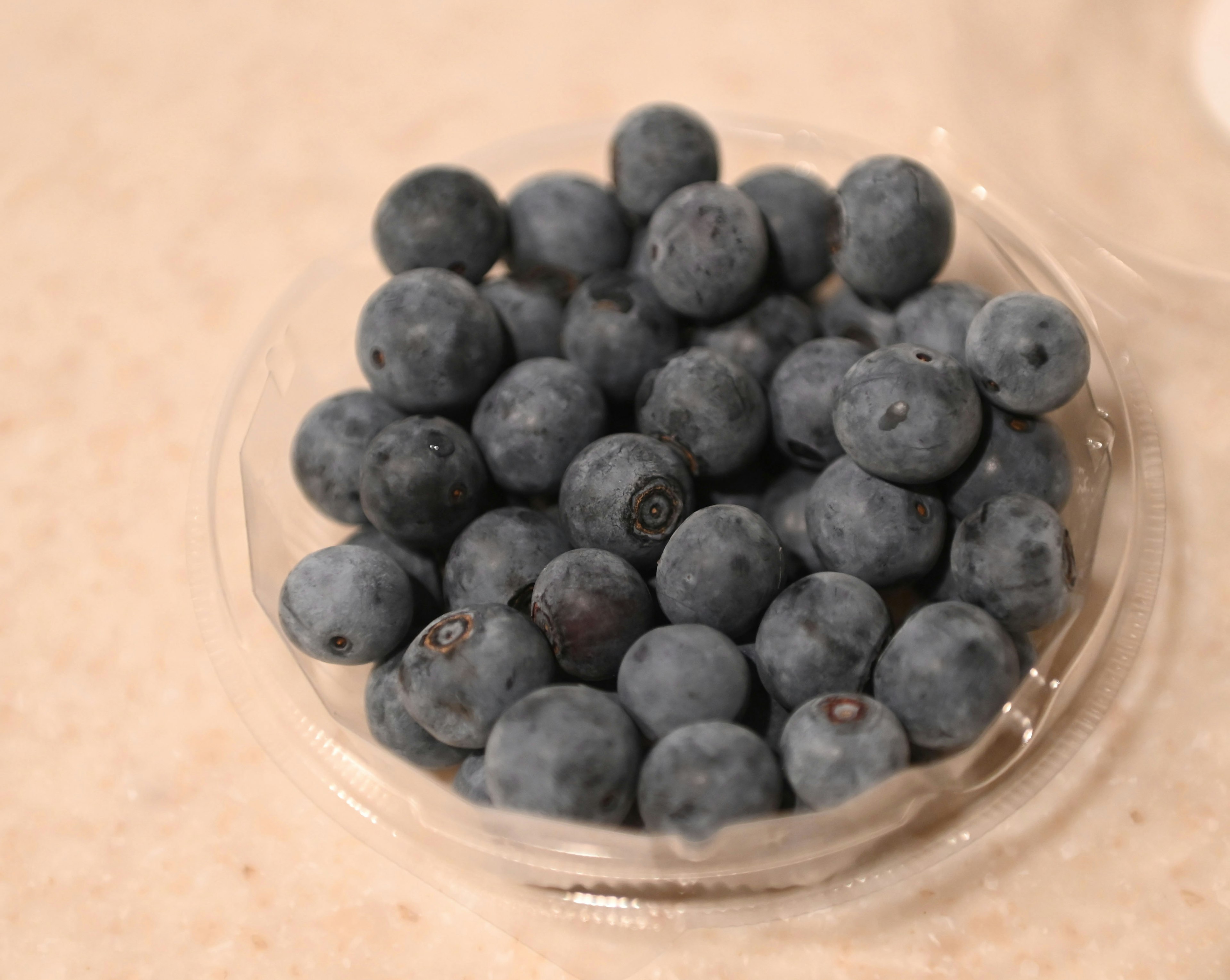 Fresh blueberries in a clear container on a light surface