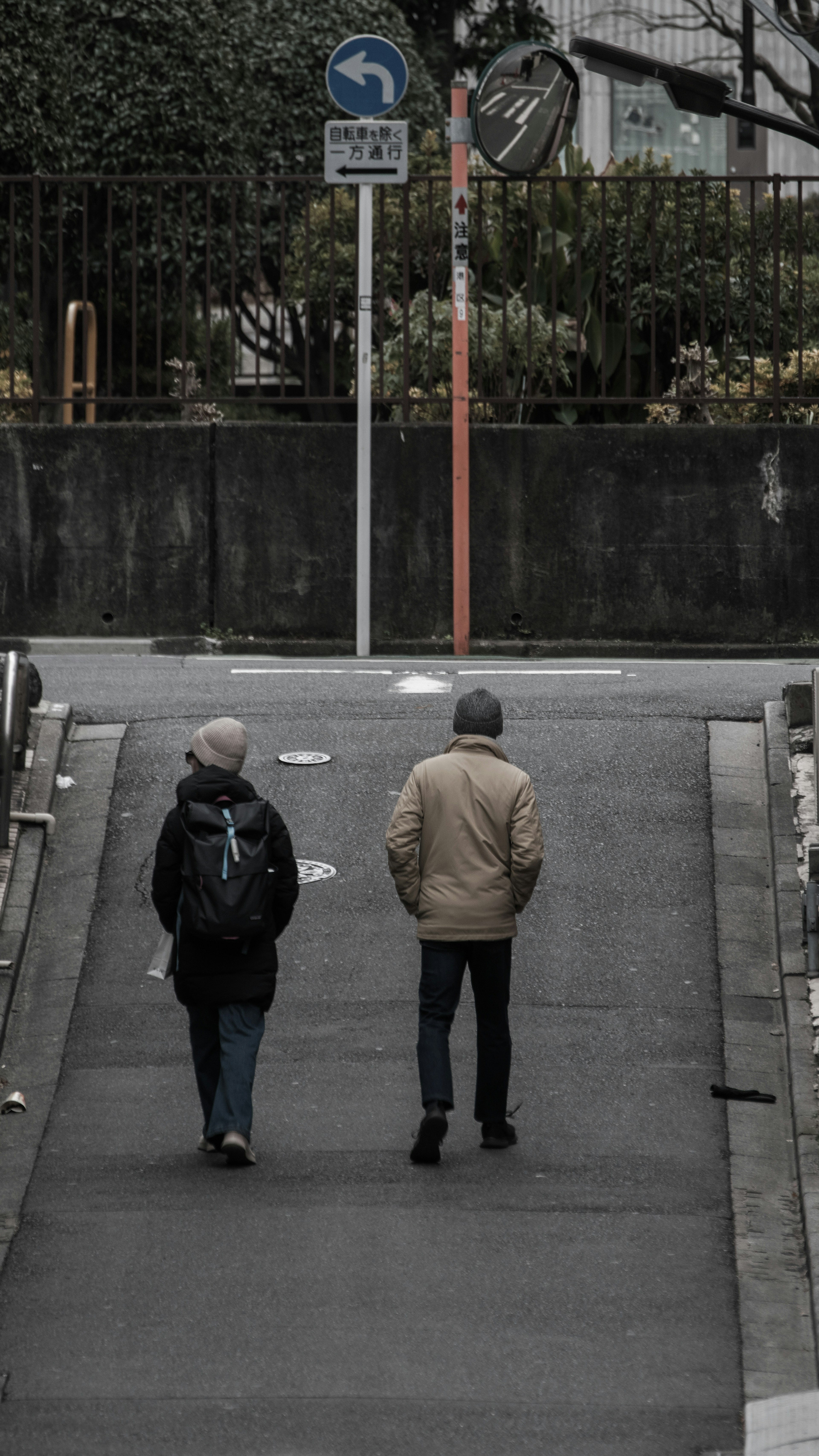 Dos personas caminando cuesta abajo con una señal de tráfico y vegetación al fondo