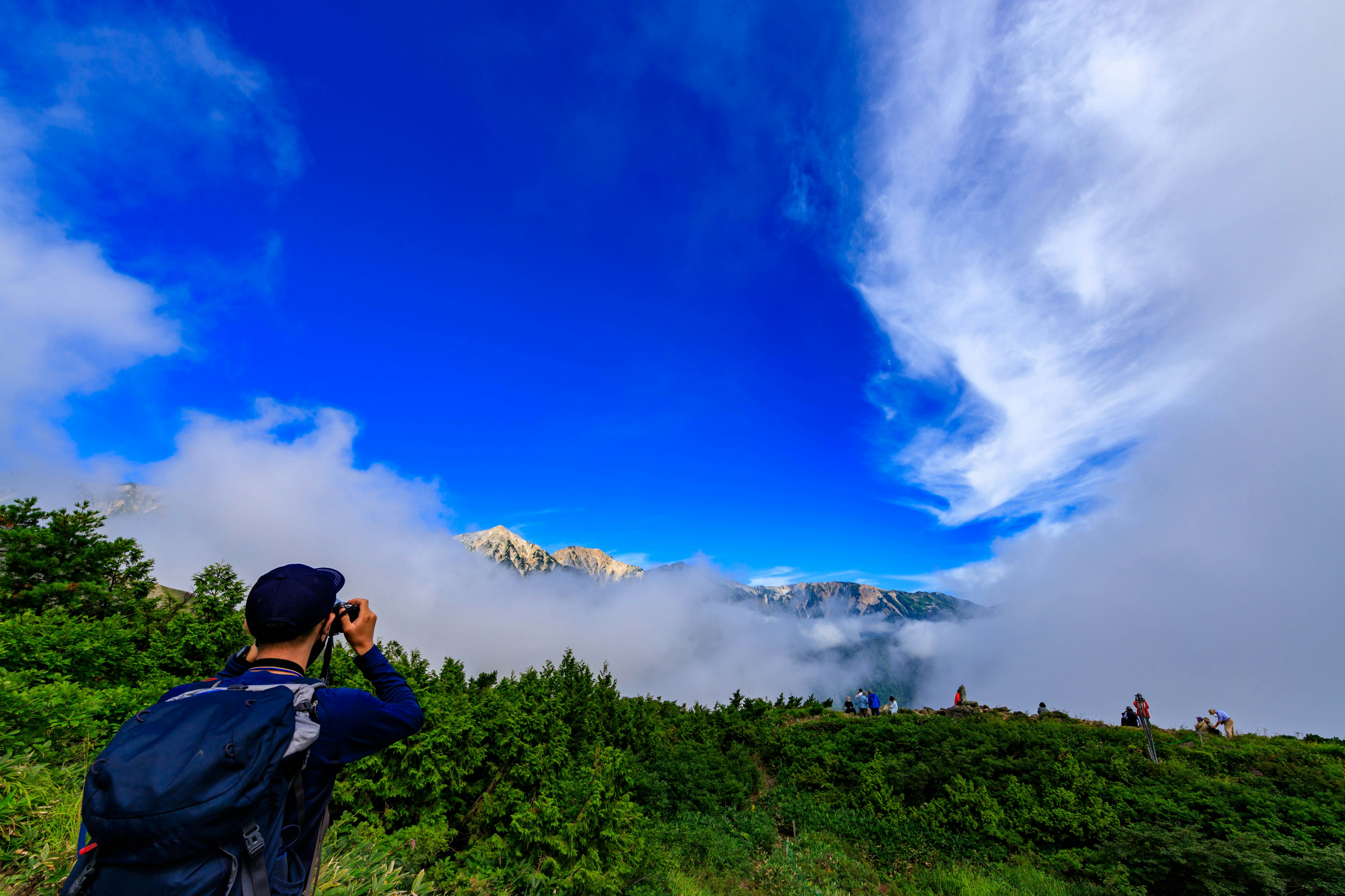 青空と雲を背景にカメラを構える人物と緑豊かな風景