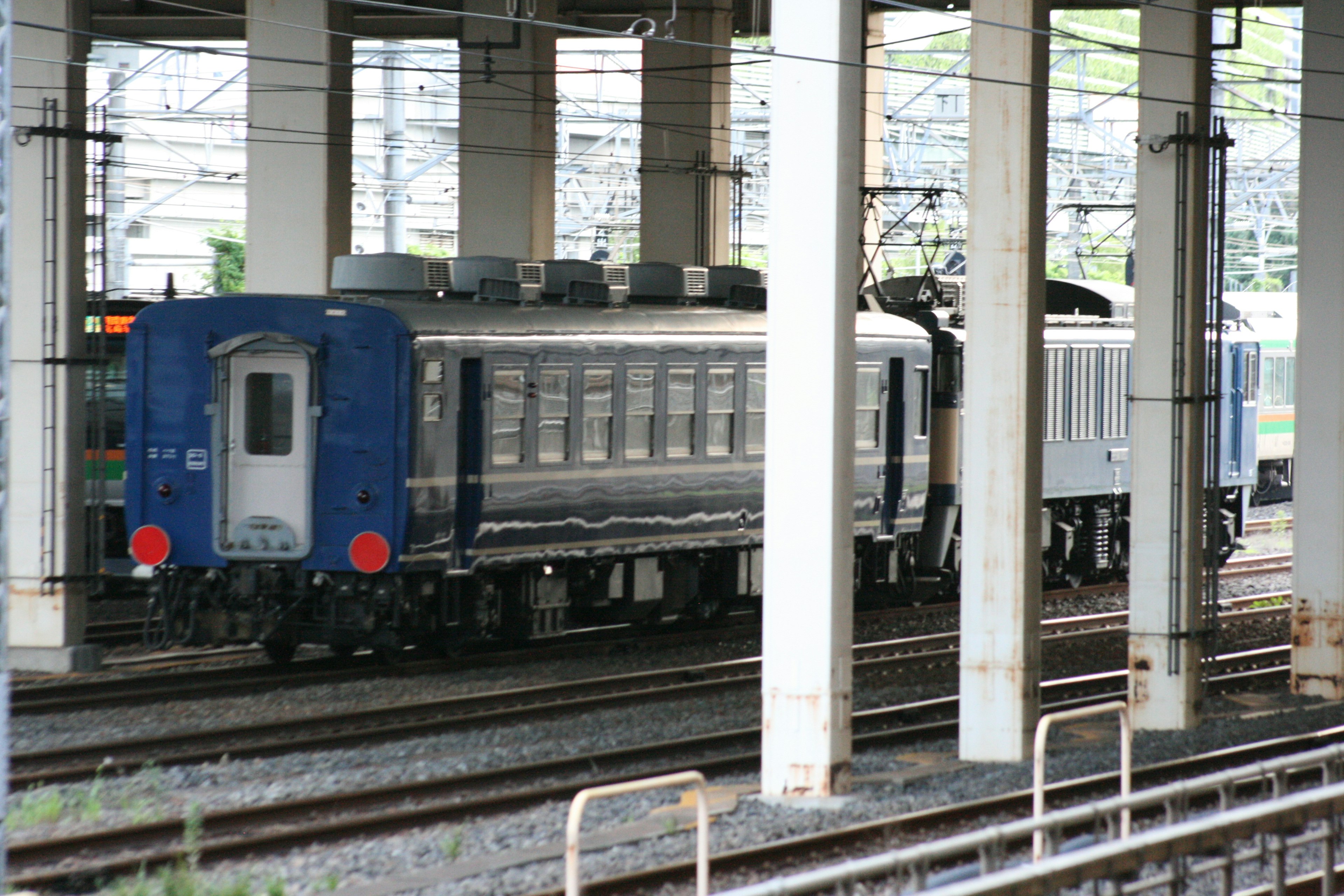 Vagón de tren azul moviéndose sobre las vías con pilares ferroviarios al fondo